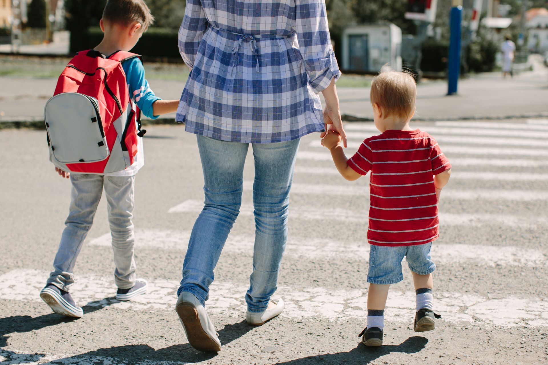 A woman is holding the hands of two children while crossing the street.