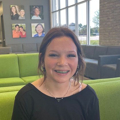 A girl with braces is smiling while sitting on a green couch