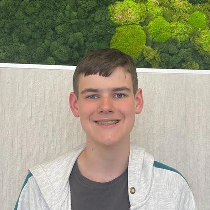 A young man is smiling in front of a moss wall.