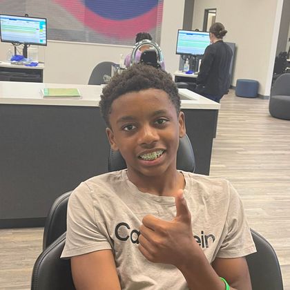 A young boy is giving a thumbs up while sitting in a chair.