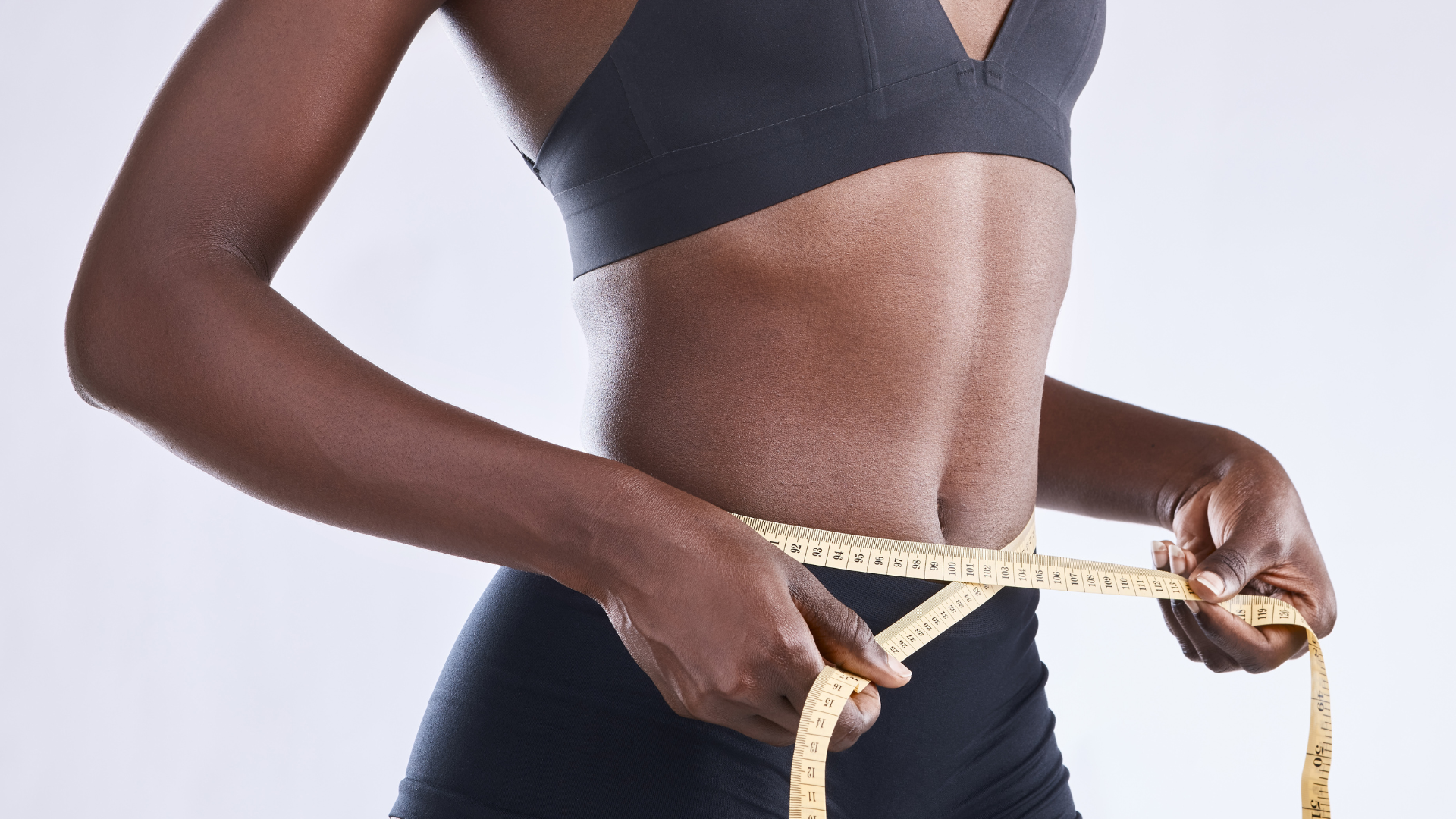 A woman is measuring her waist with a tape measure.