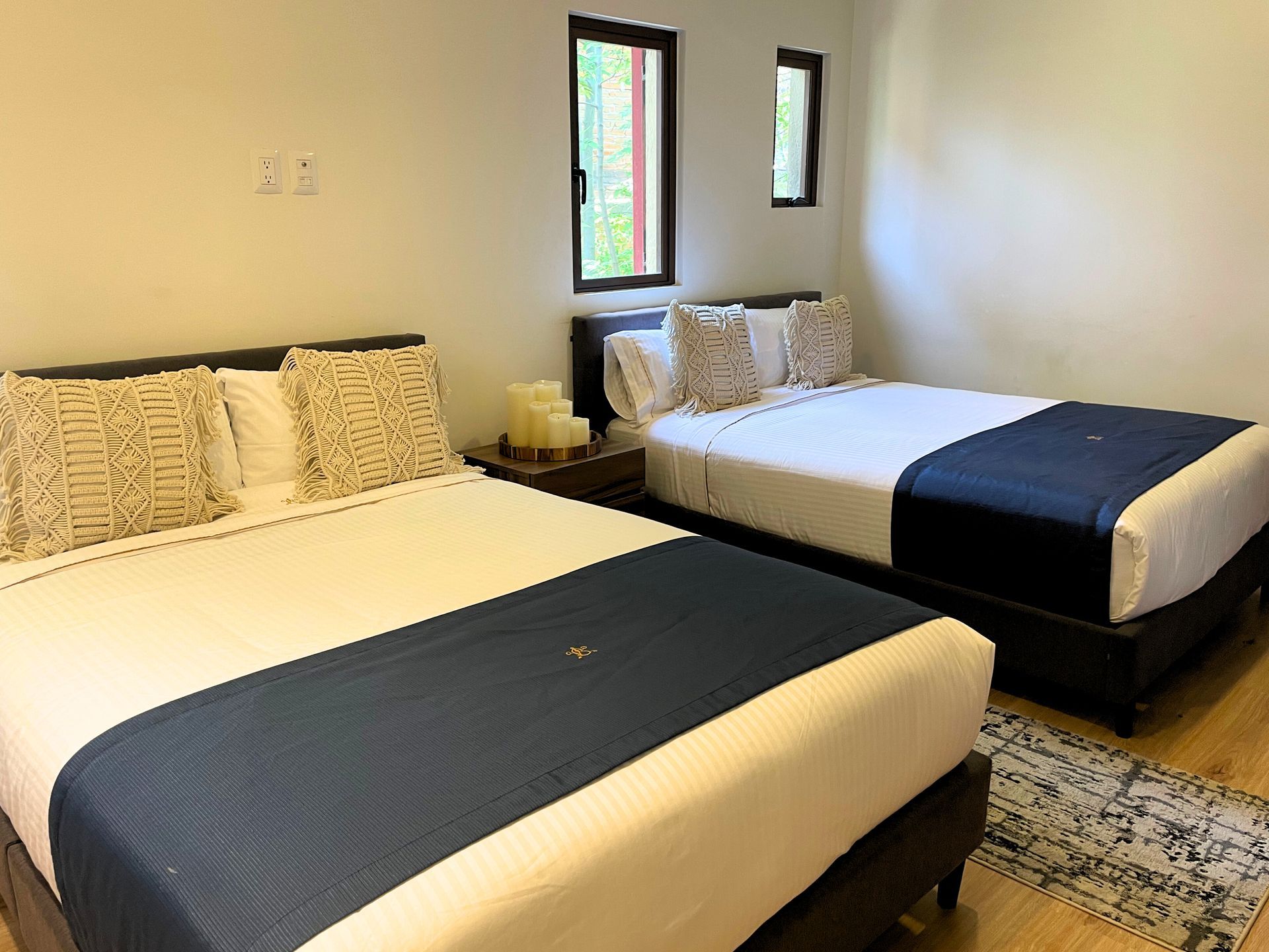Two neatly made beds in a simple hotel room with white walls and a patterned rug.