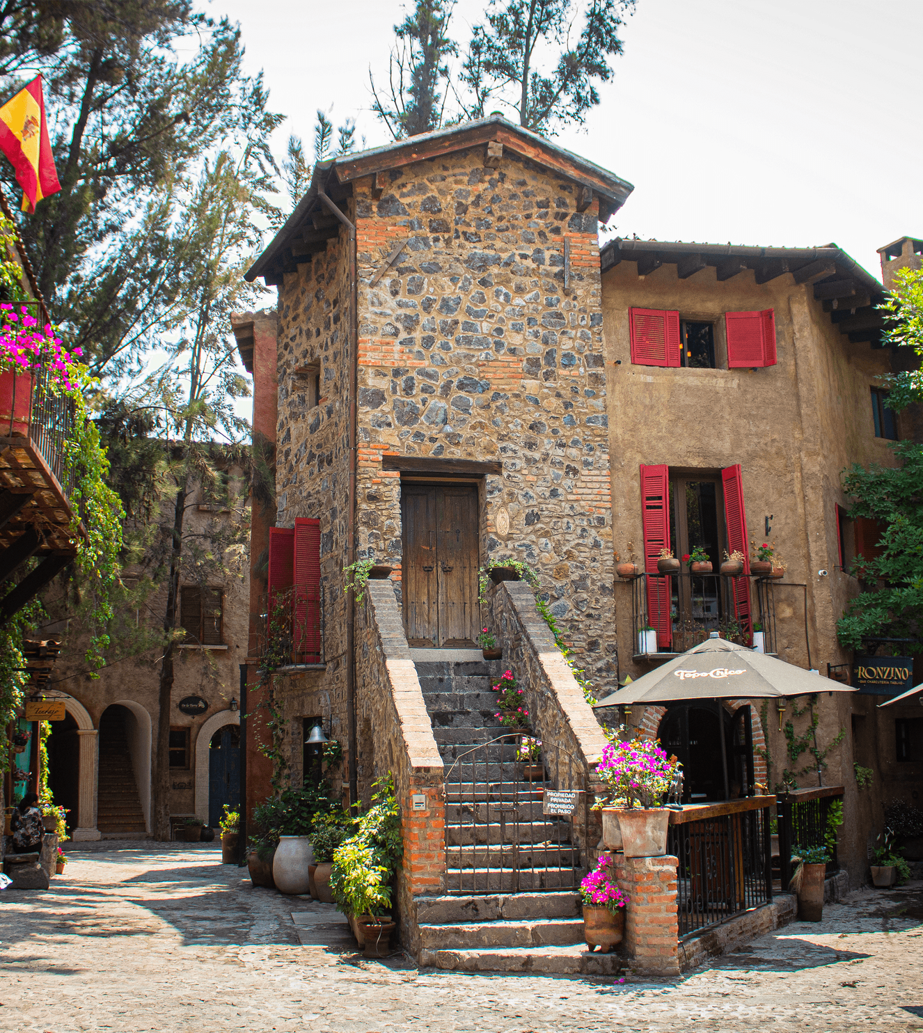 Stone building with red shutters, flower pots, and a Spanish flag.