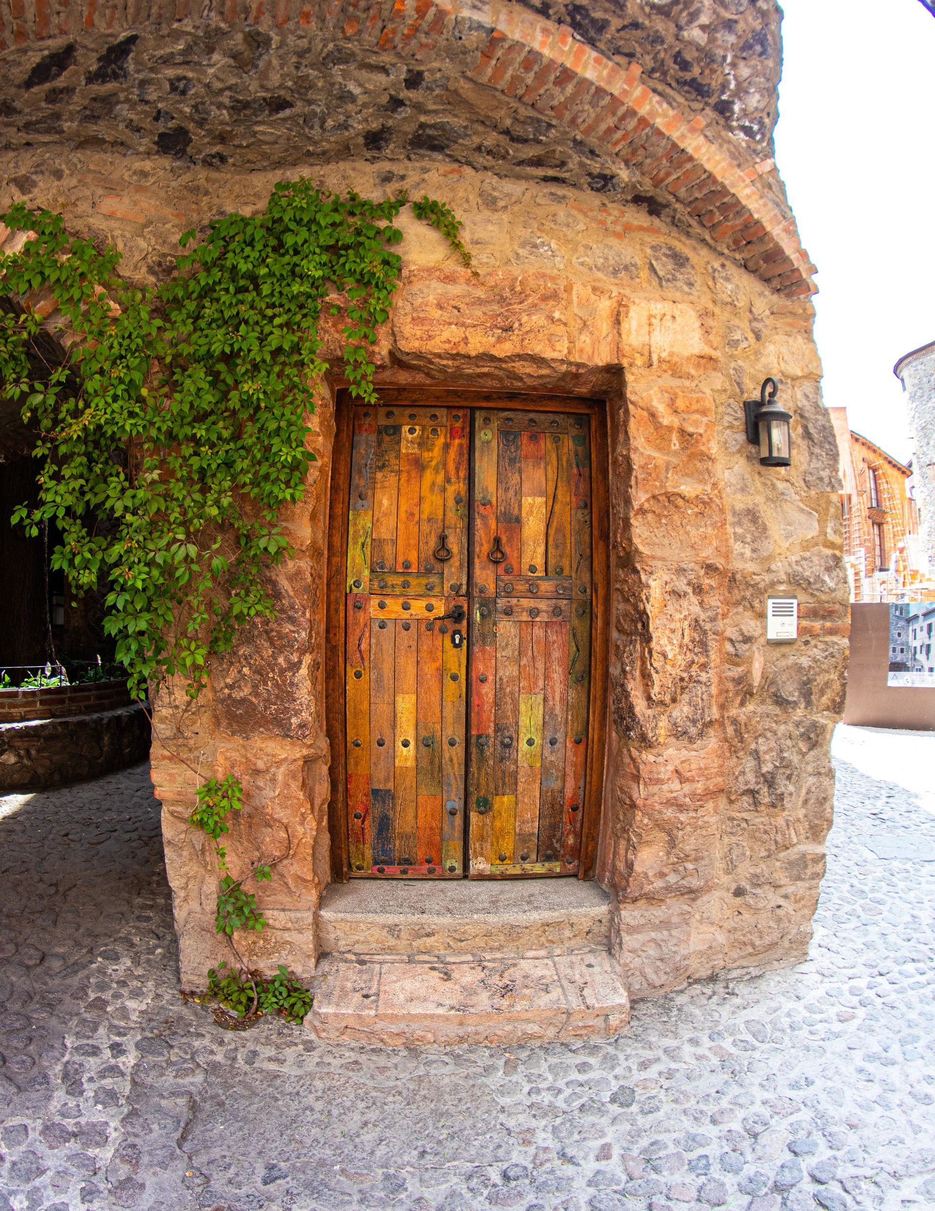 Stone doorway with weathered, colorful wooden door, ivy, and cobblestone path.