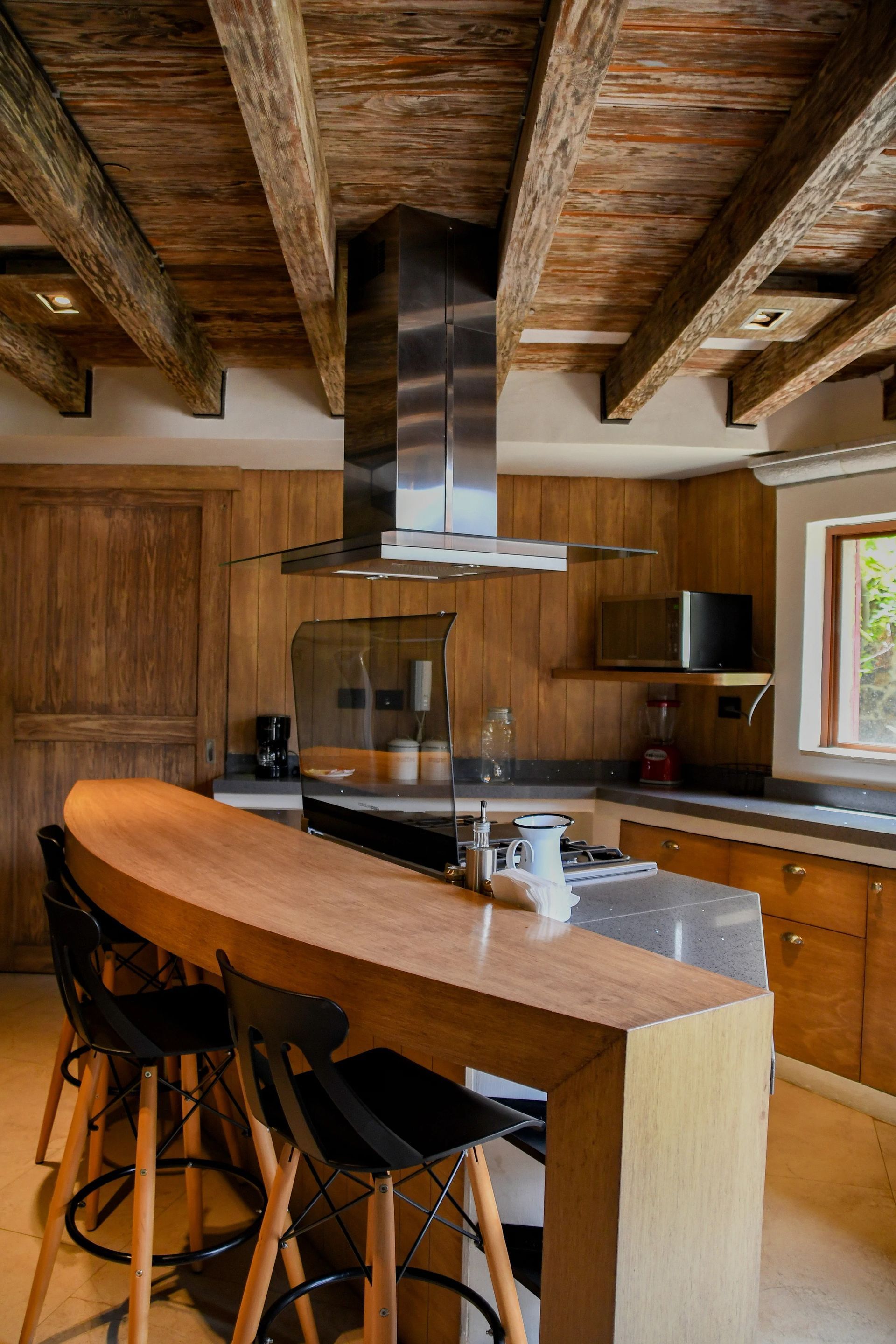 Kitchen with wooden beams, island bar, stainless steel hood, and stools.