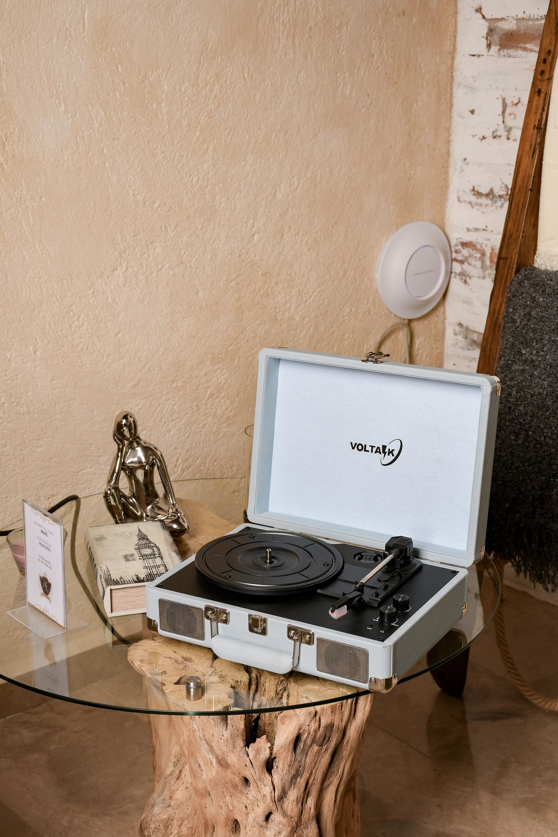 Record player on a glass table with a wooden base; Buddha statue, neutral wall in the background.