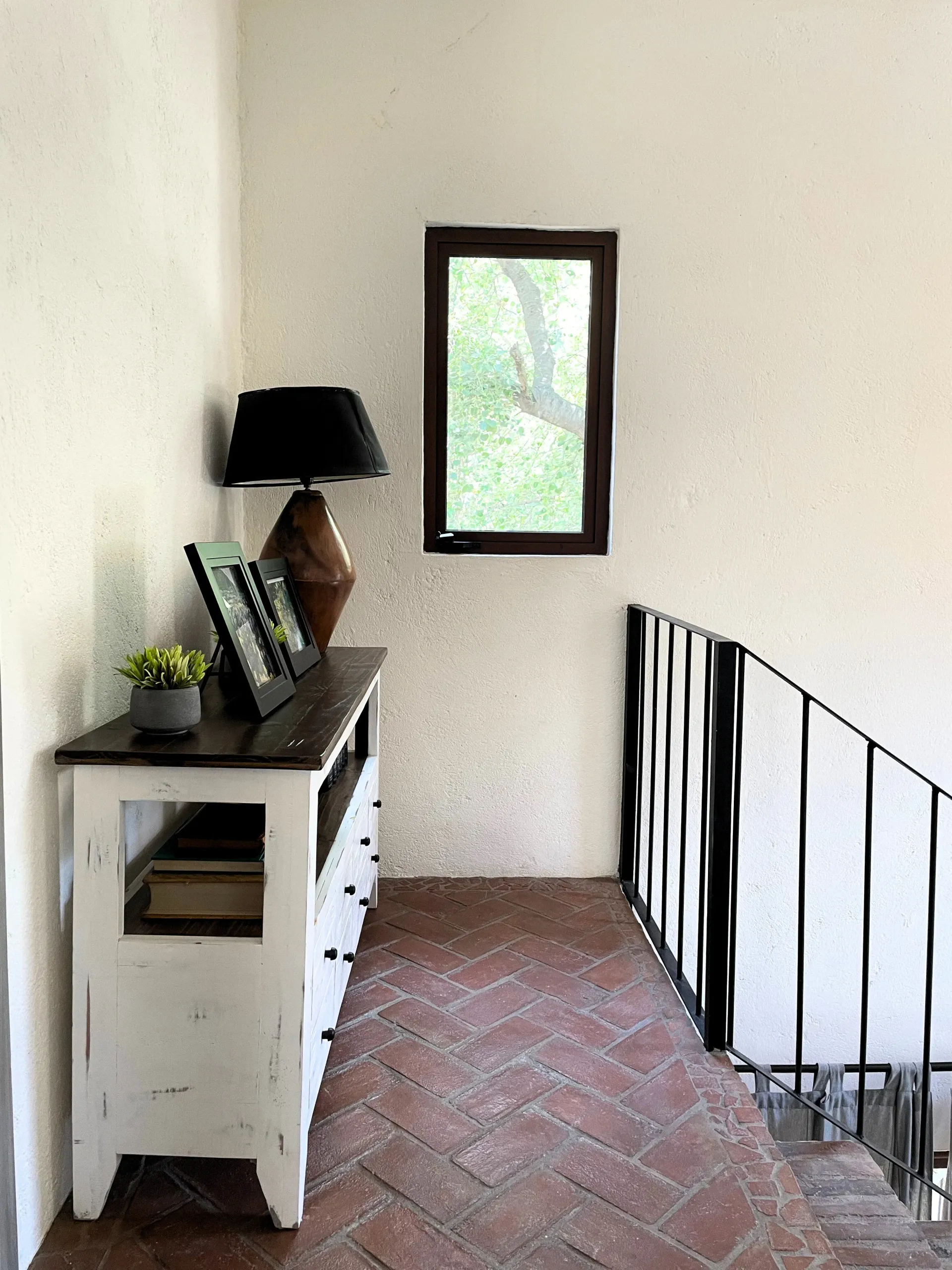 Hallway with white and brown console table, lamp, window, and brick floor.