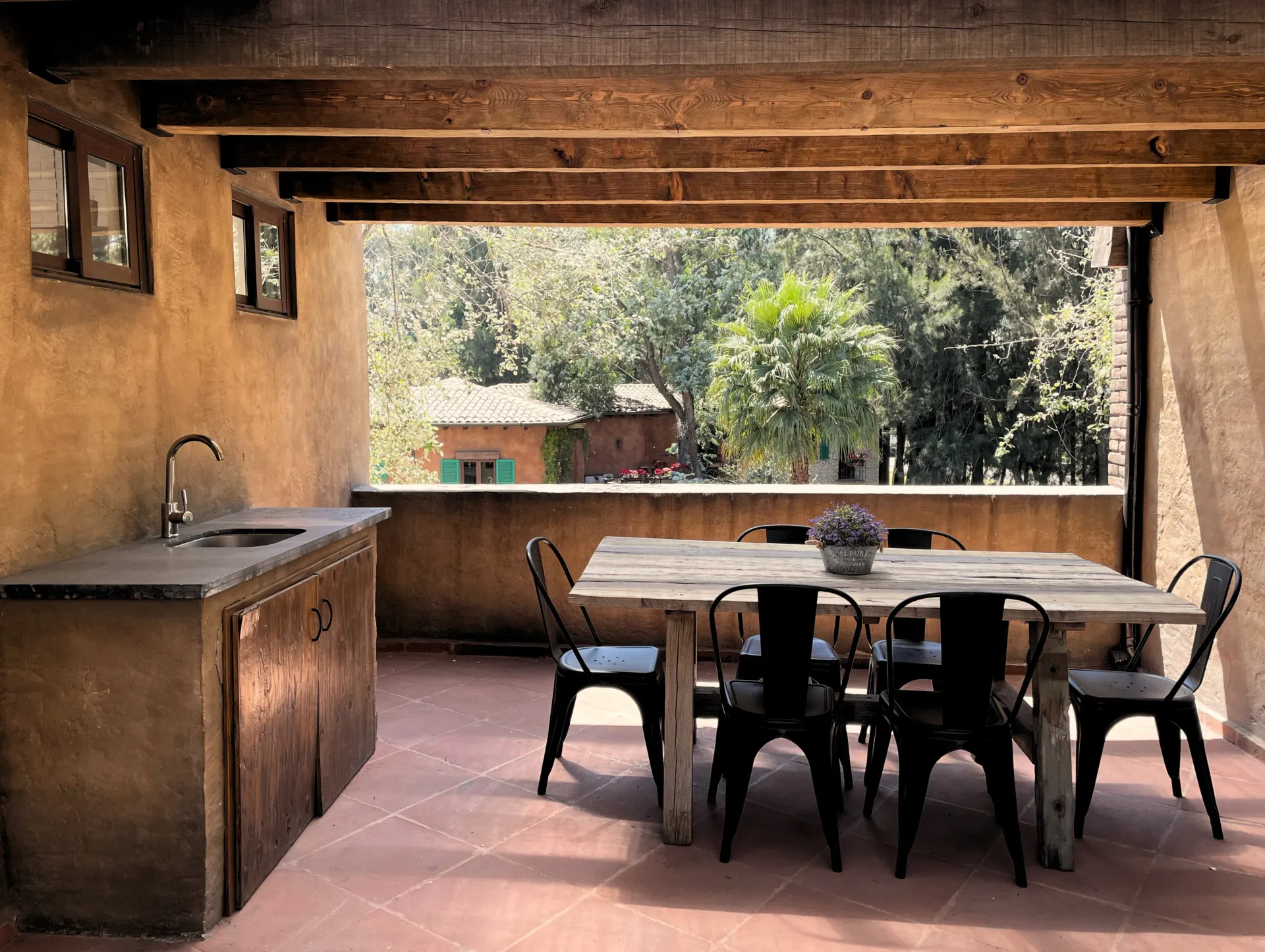 Covered patio with dining table and sink, overlooking trees and a building.