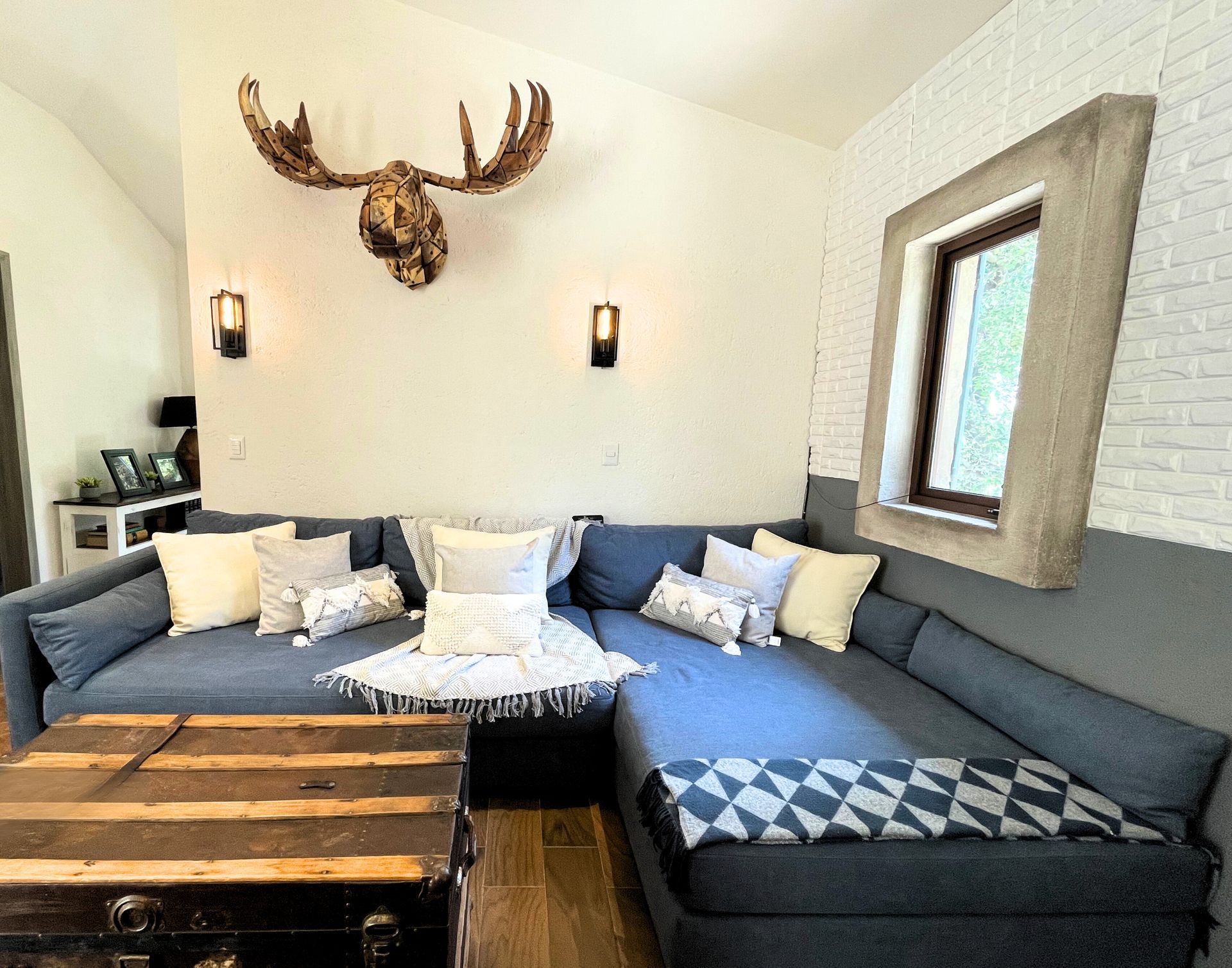 Cozy living room with a gray sectional, rustic wood coffee table, moose wall decor, and wall sconces