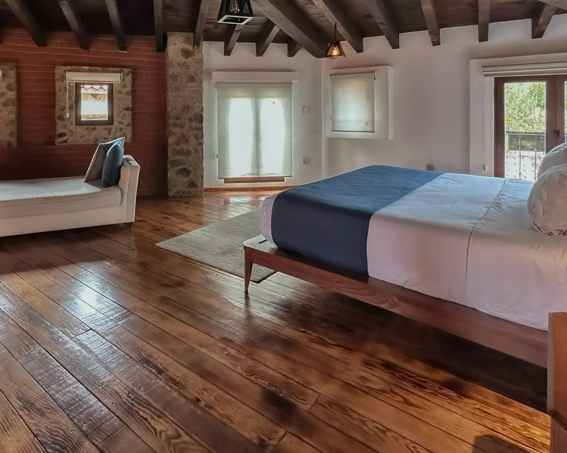 Bedroom with hardwood floor, bed, sofa, stone wall, and French doors.
