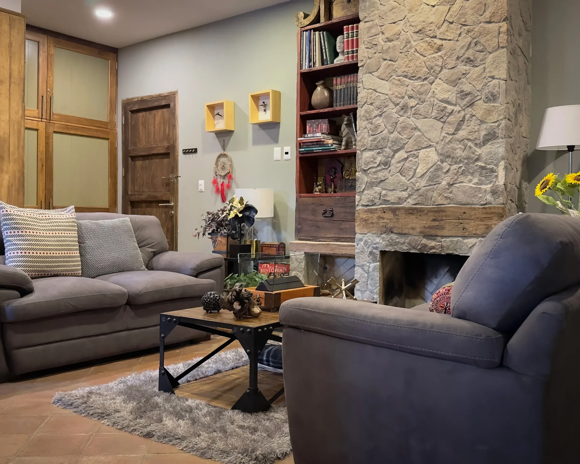 Cozy living room with gray sofas, stone fireplace, wooden accents, and decor.