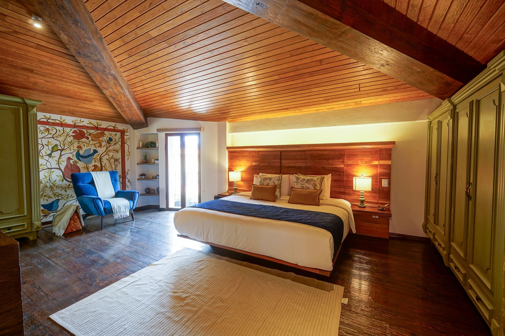Cozy bedroom with a bed, wooden vaulted ceiling, tiled floor, and green wardrobes along the wall
