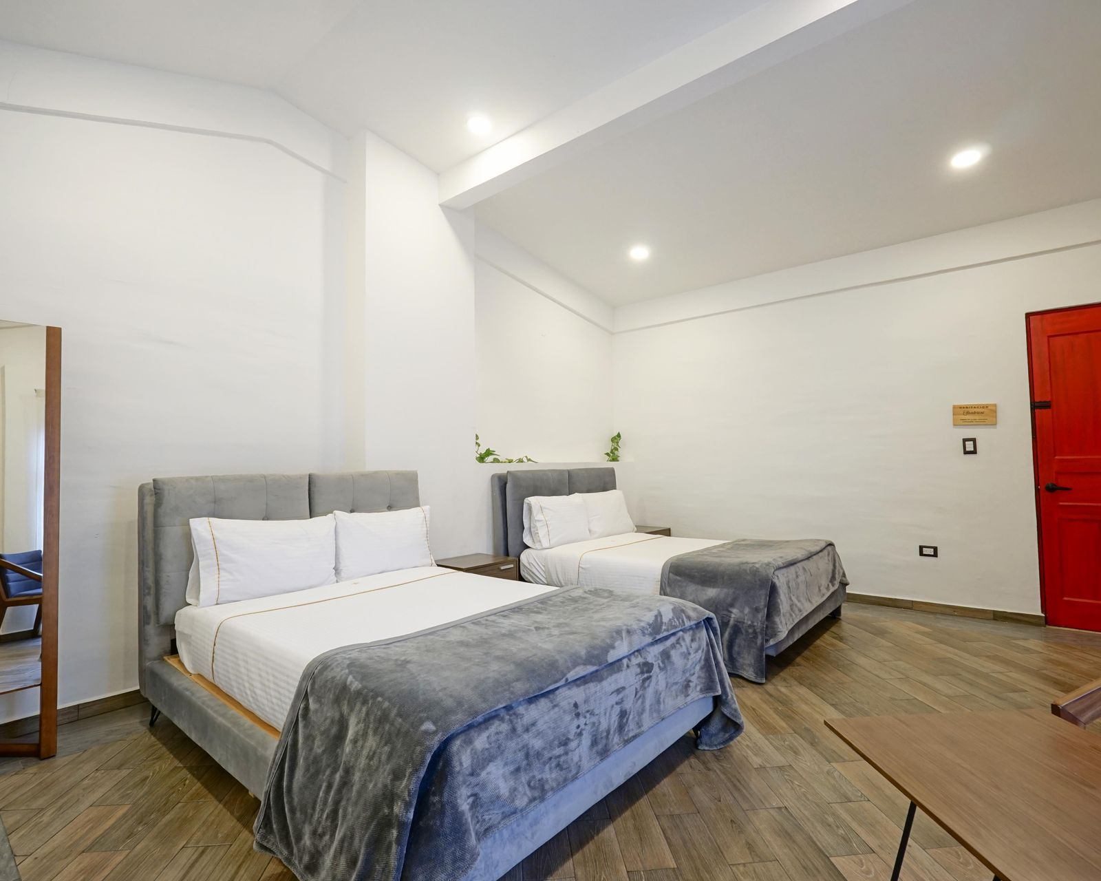 Dormitorio con ropa de cama blanca, cabecero gris, armario blanco y puerta rojo oscuro.