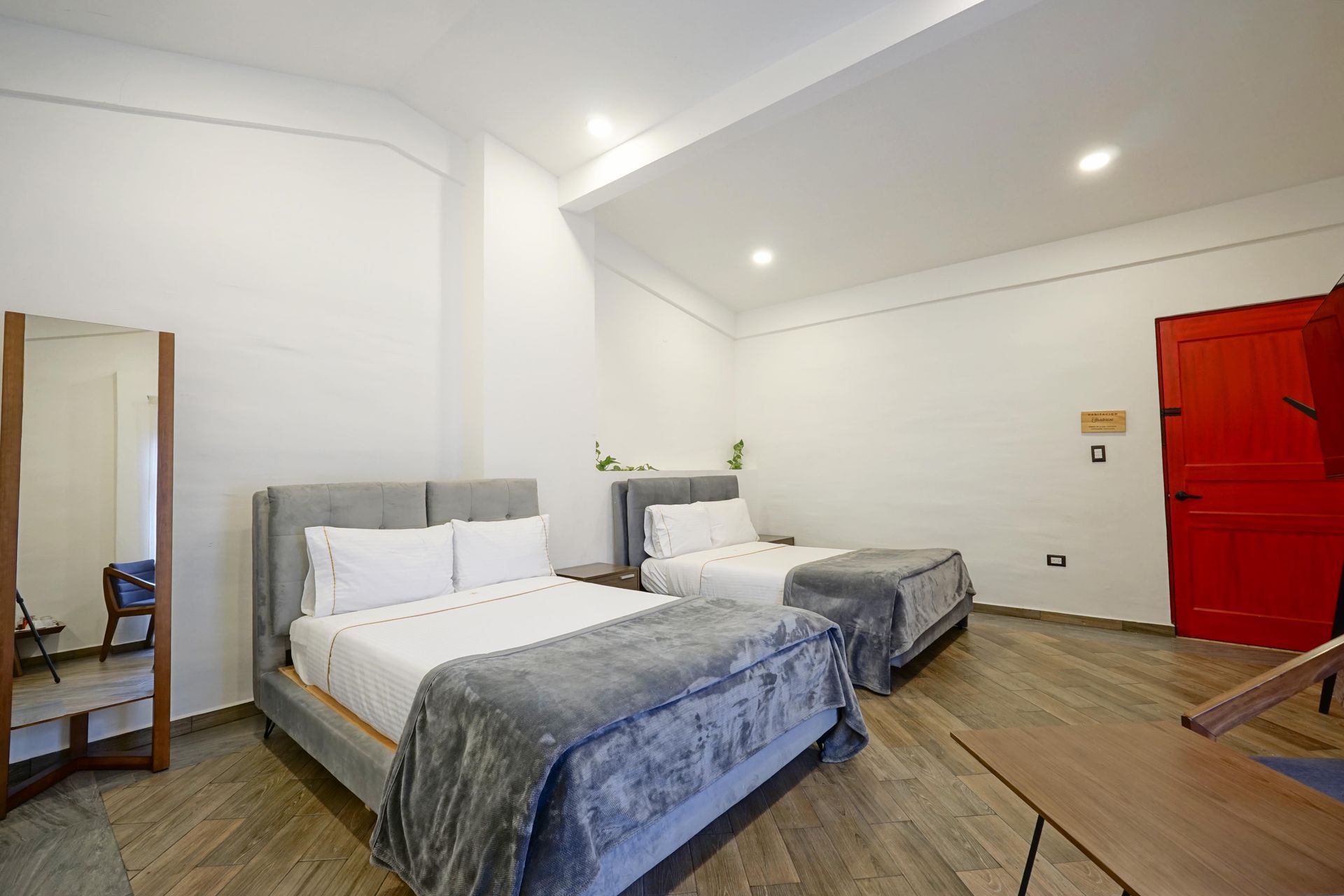Dormitorio con ropa de cama blanca, cabecero gris, armario blanco y puerta rojo oscuro.