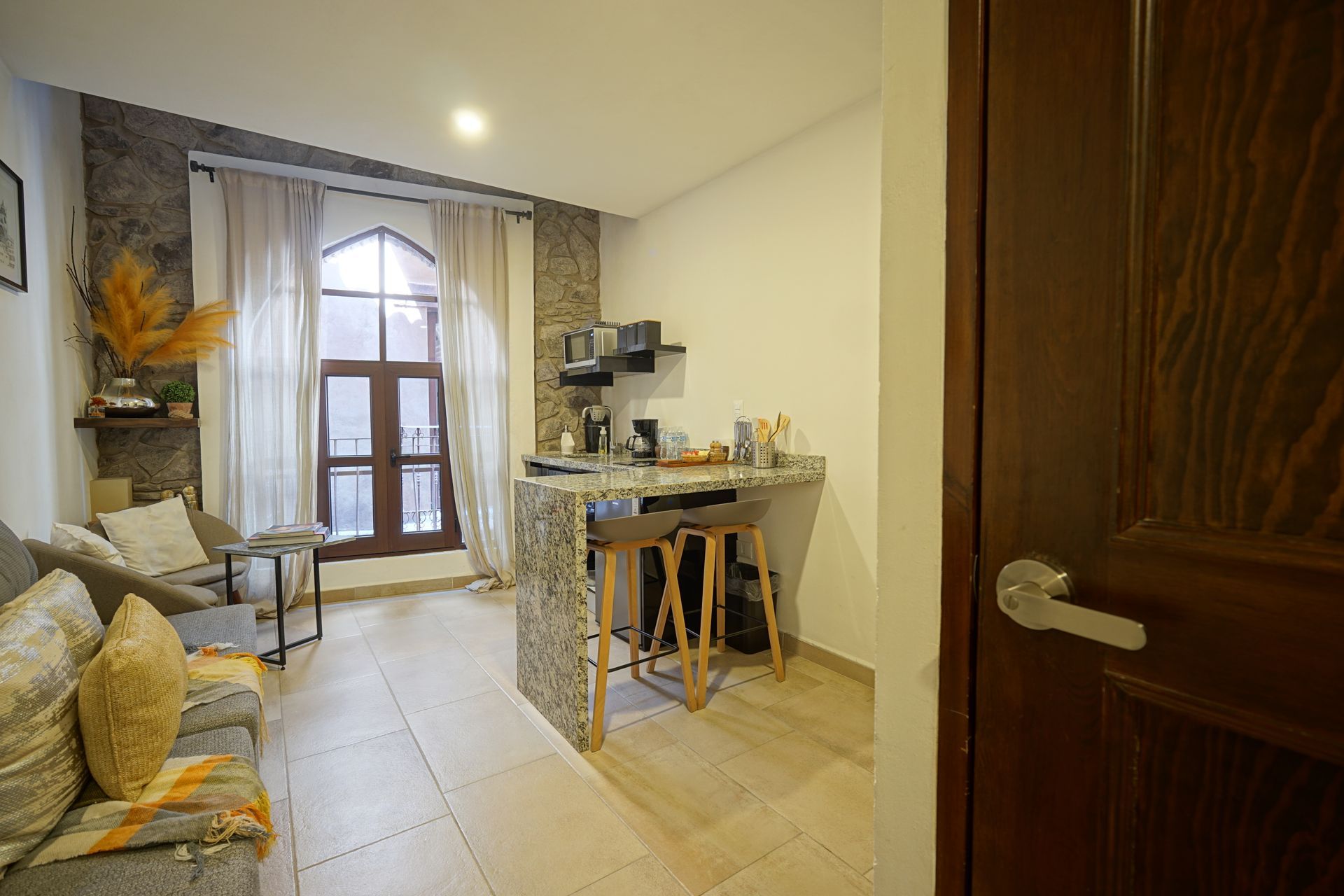 Dormitorio con cama, cabecero decorativo, suelo de madera, escaleras y puerta abierta a la izquierda.