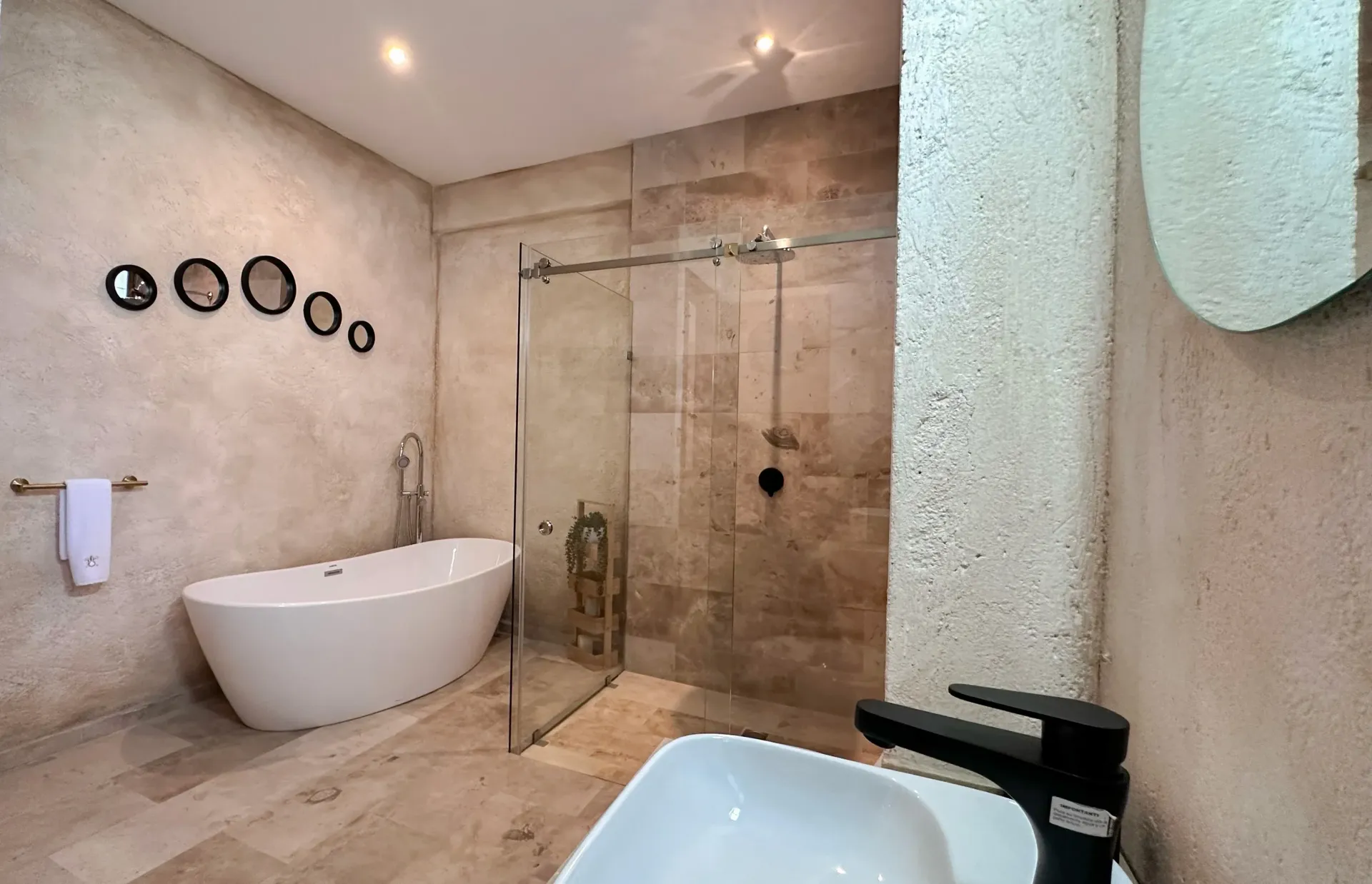 Modern bathroom with a white tub, glass shower, and round mirrors on a textured wall.