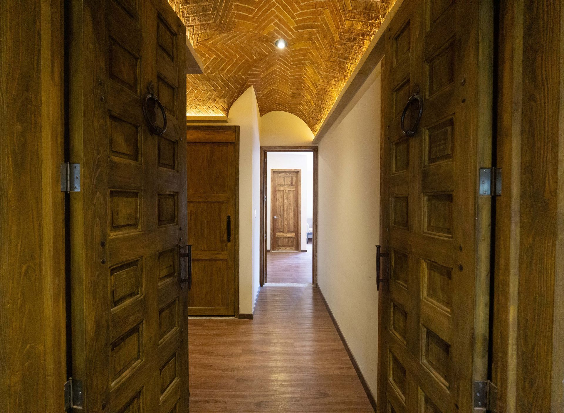 Wooden doors open to a hallway with arched brick ceiling, leading to other doorways.