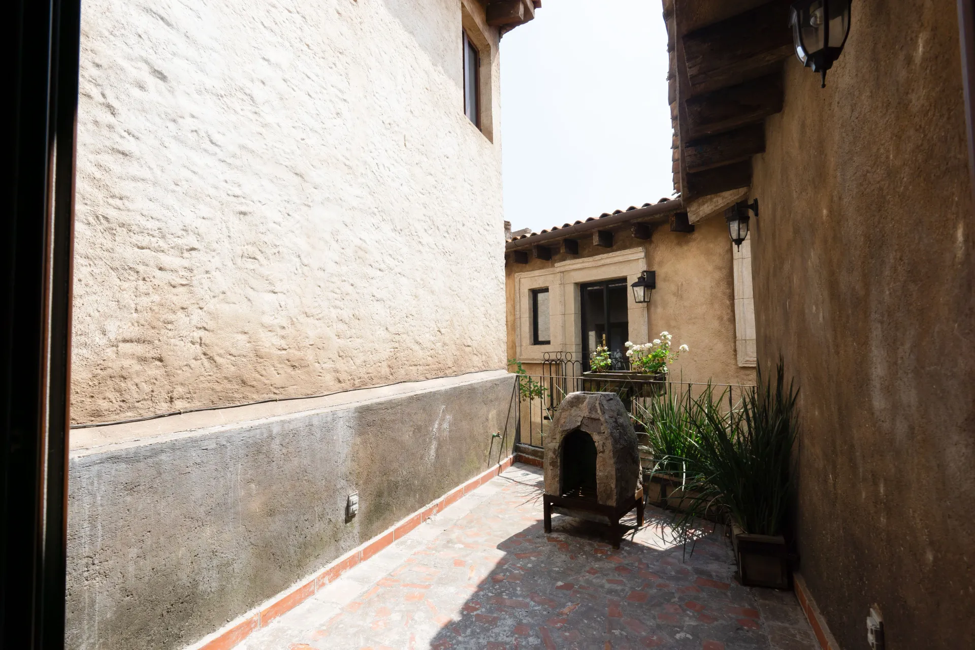 Narrow outdoor space between buildings; stone walls, red tile ground, and a small stone fire pit.
