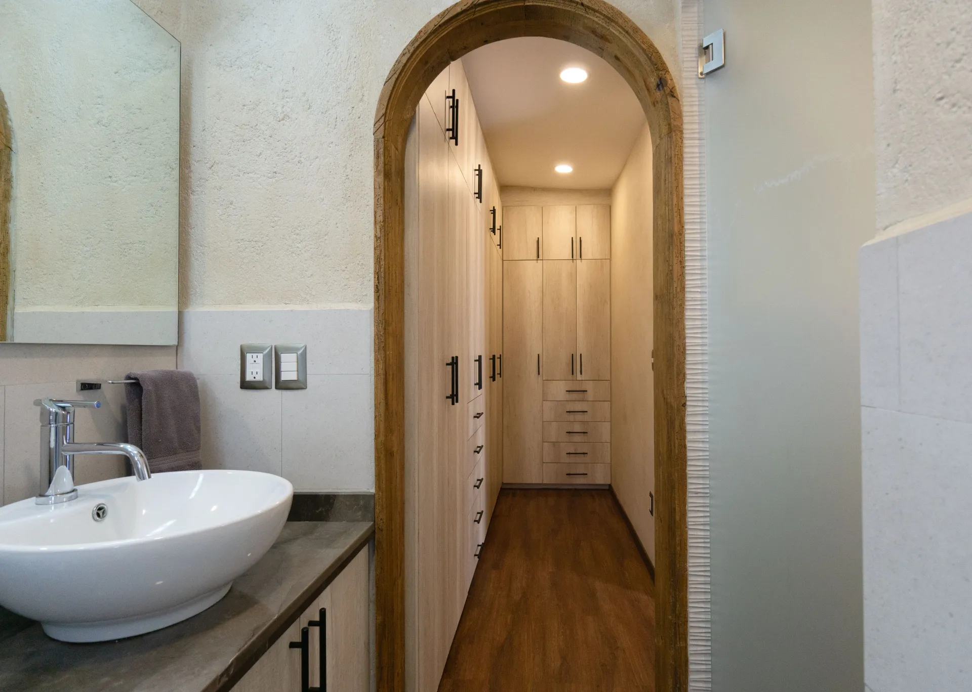Bathroom with sink and arched doorway leading to a closet with wooden floors.
