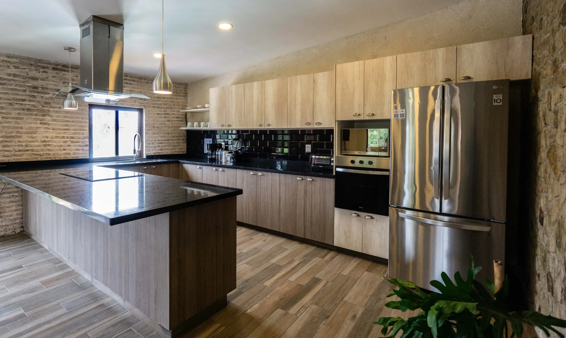 Modern kitchen with wood cabinets, black countertops, and stainless steel refrigerator.