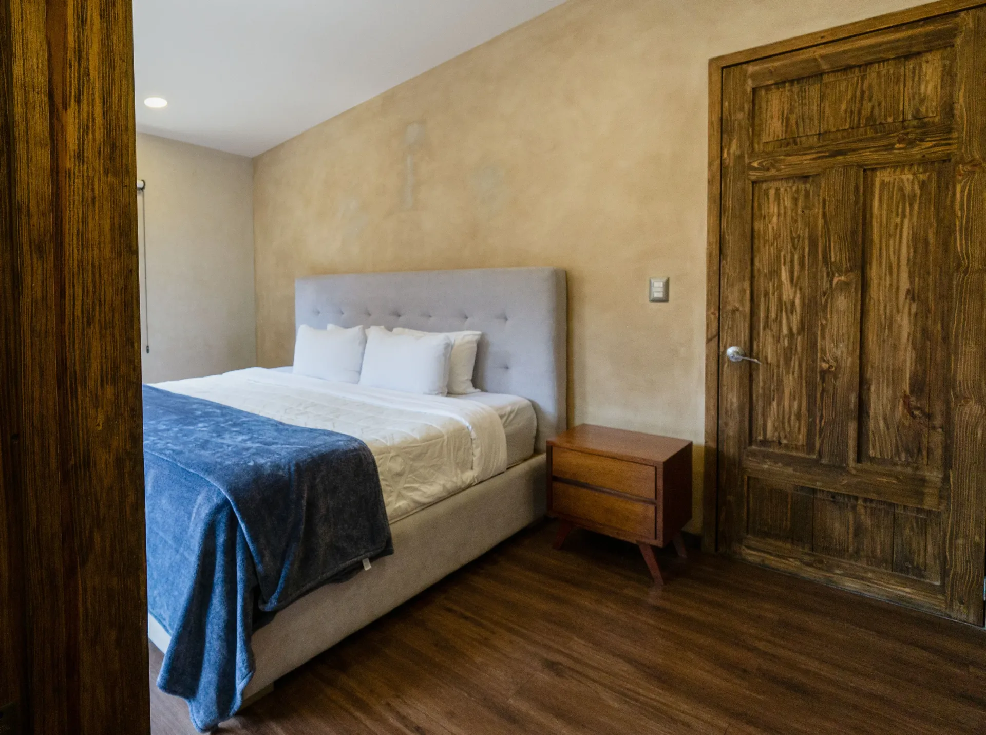 Bedroom with a bed, nightstand, and wooden door, brown floors, and beige walls.