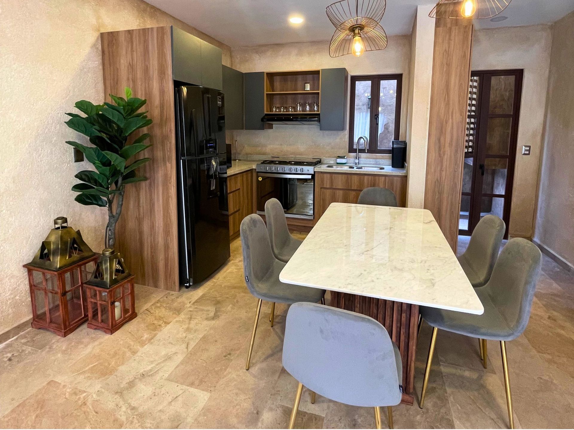 Modern kitchen and dining area with wooden table, gray chairs, and potted plant near black refrigerator.