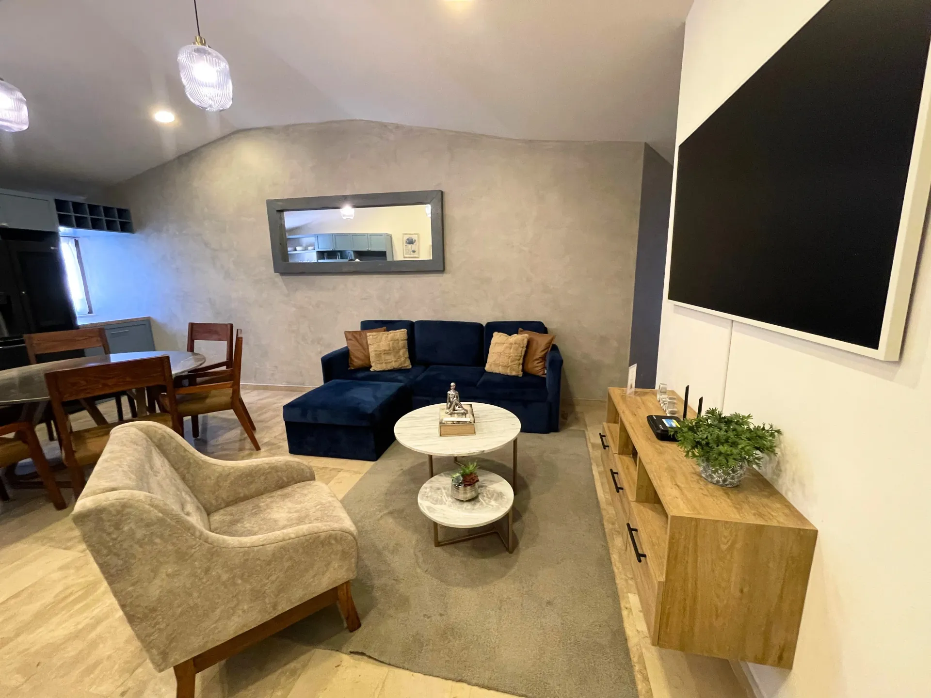 Living room with navy blue couch, accent chair, coffee table, and large TV on a wood console.