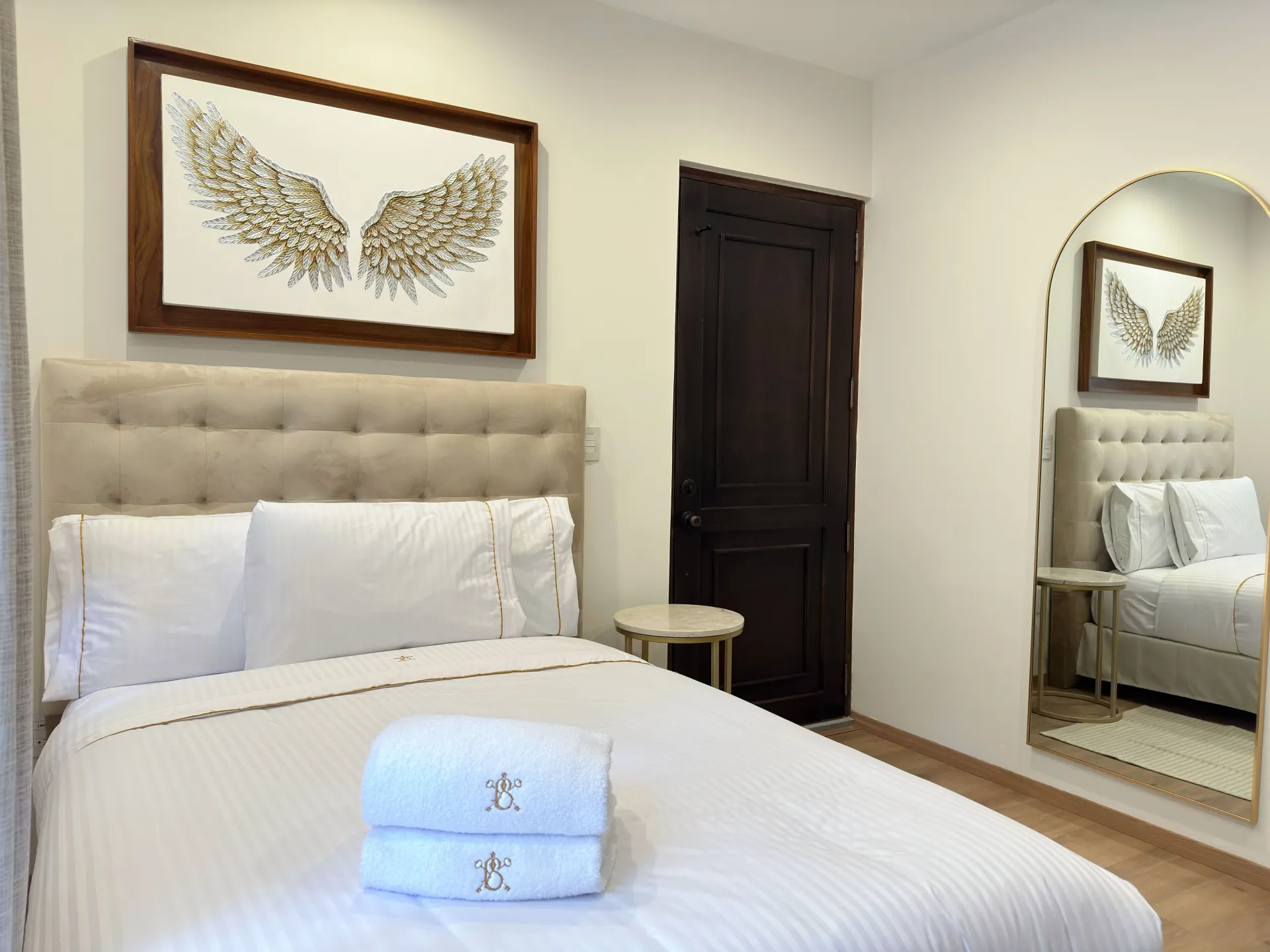 Bedroom with bed, art, mirror, and dark wooden door. Neutral tones, clean design.