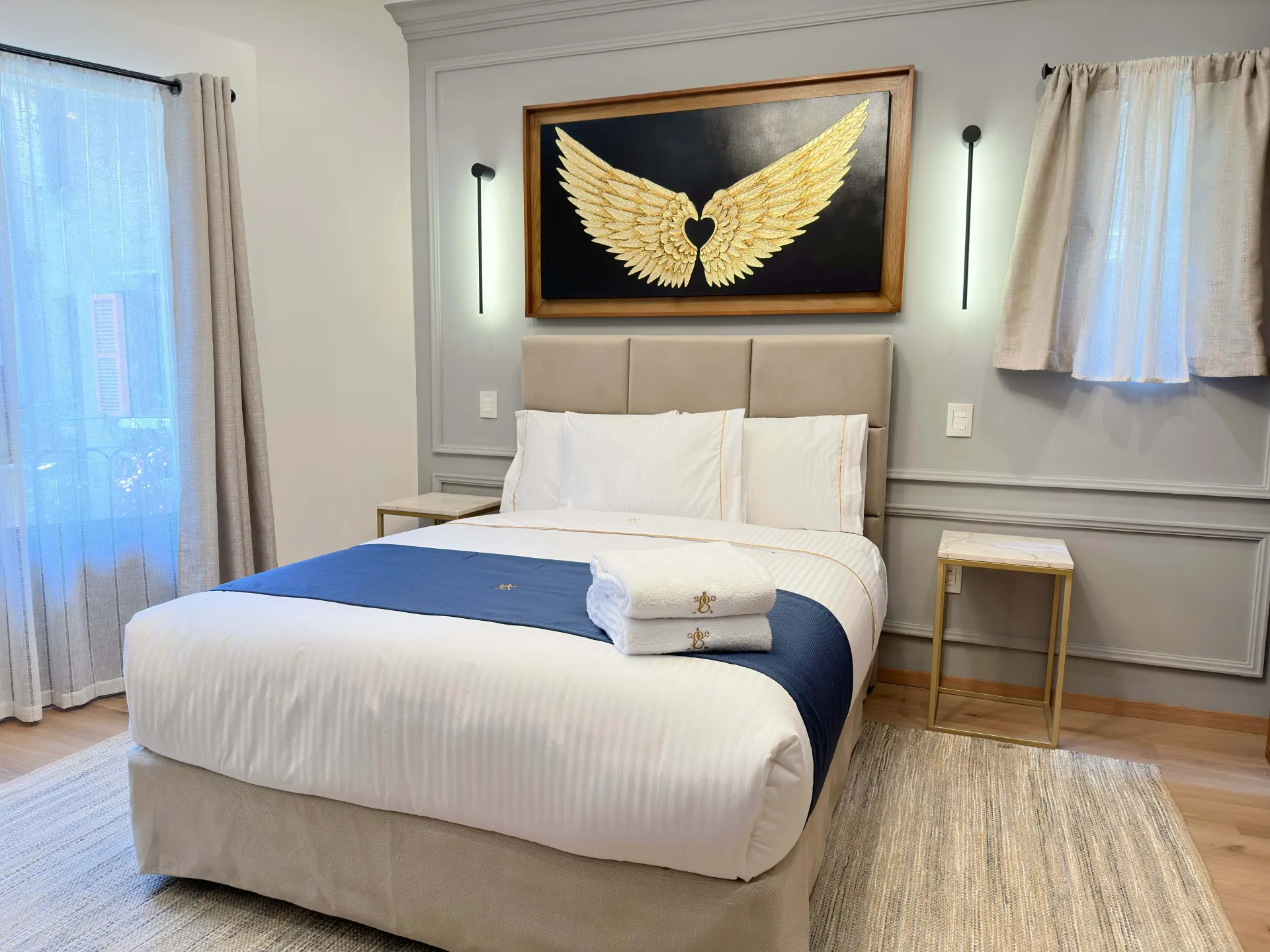 Bedroom with a queen-sized bed, artwork of gold wings, and neutral color palette.
