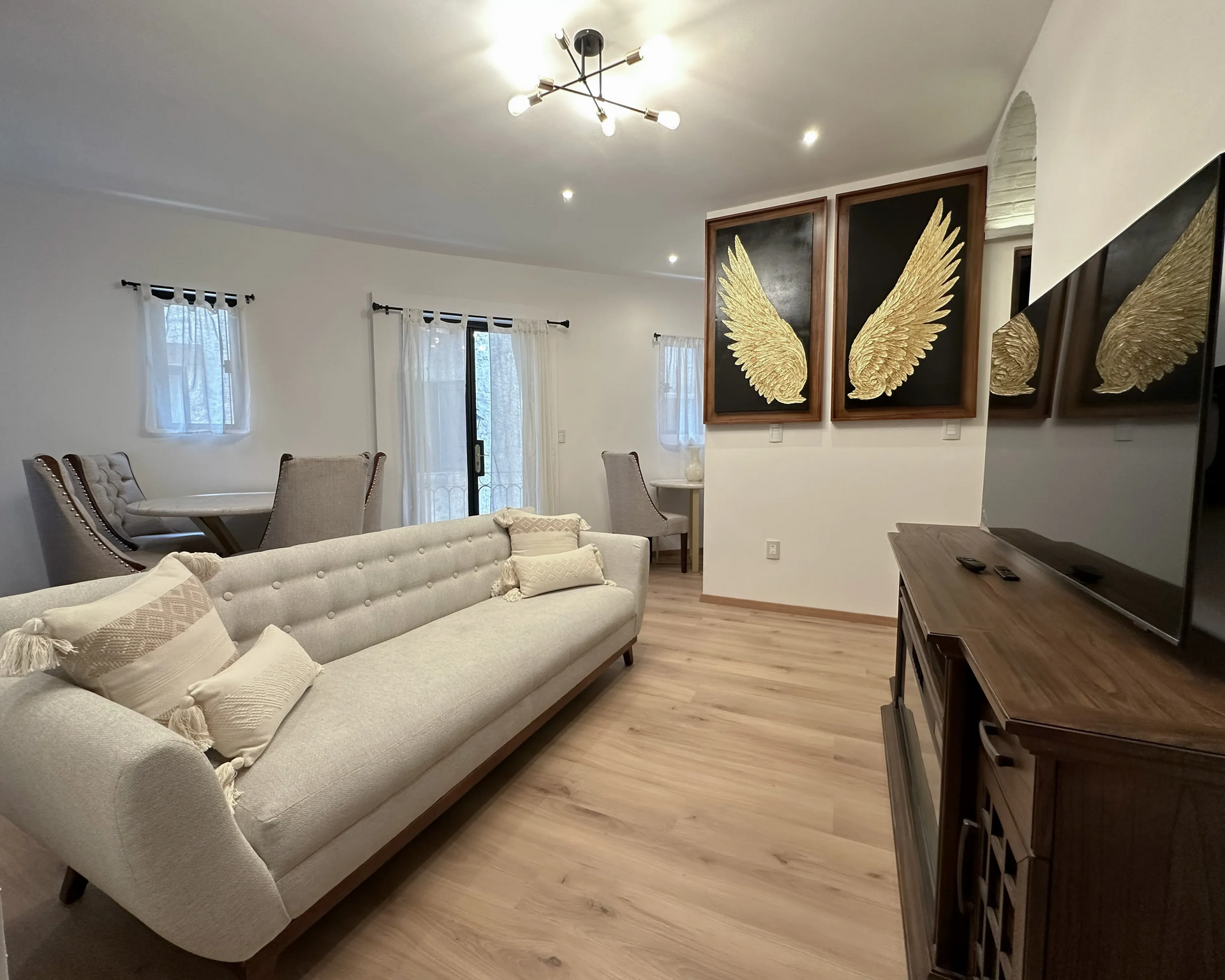 Sala de estar con sofá, mesa de comedor, obras de arte y televisión. Tonos neutros y luminosos, con suelo de madera.