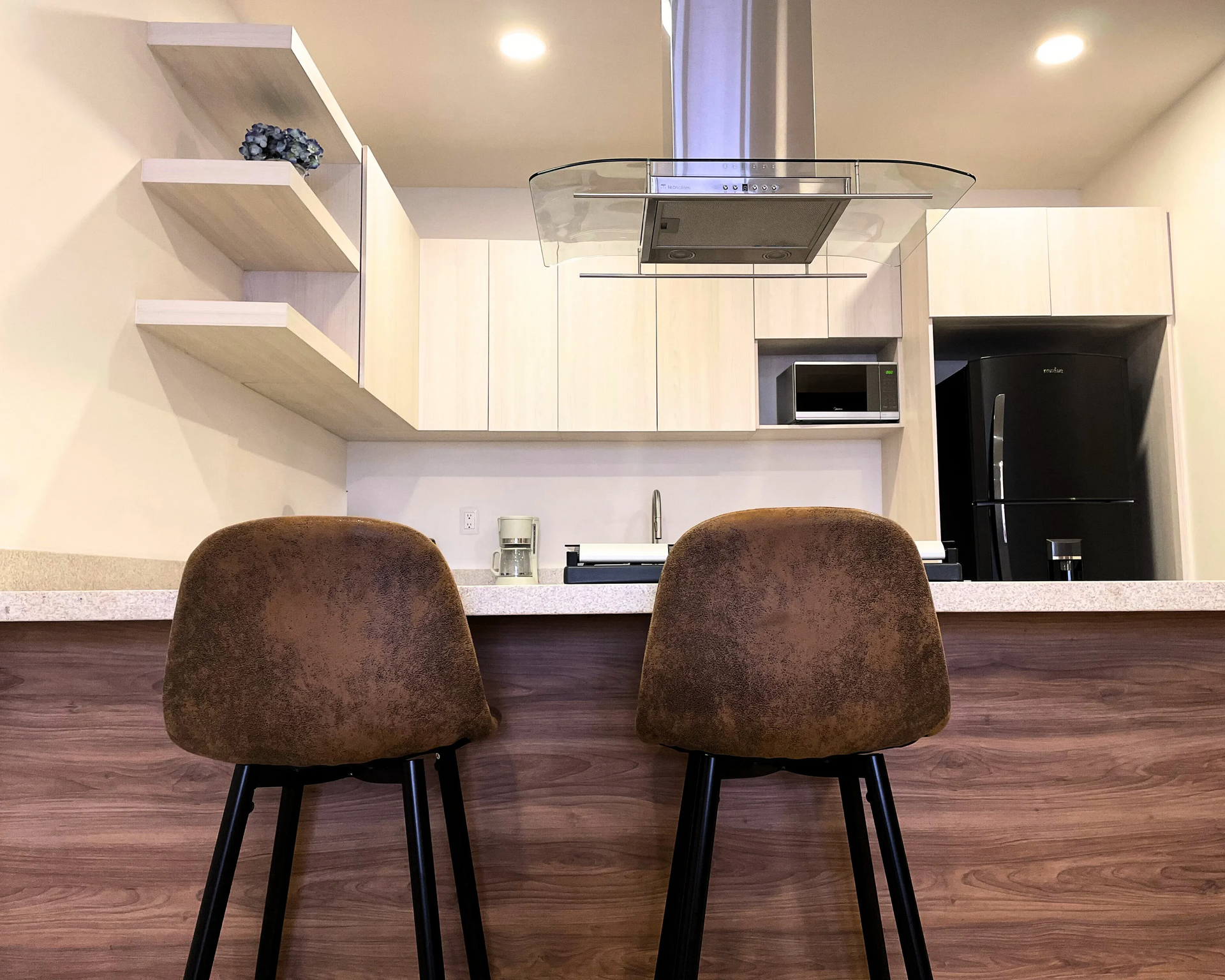 Dos taburetes de bar marrones en una cocina moderna con gabinetes claros, un refrigerador negro y una campana extractora