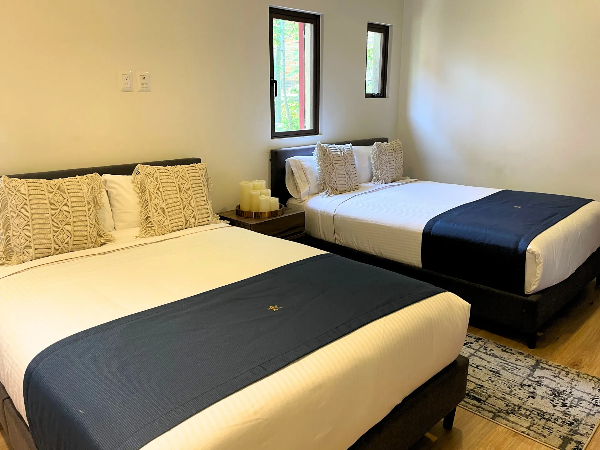 Two queen beds in a hotel room with blue bed runners, windows, and a rug.