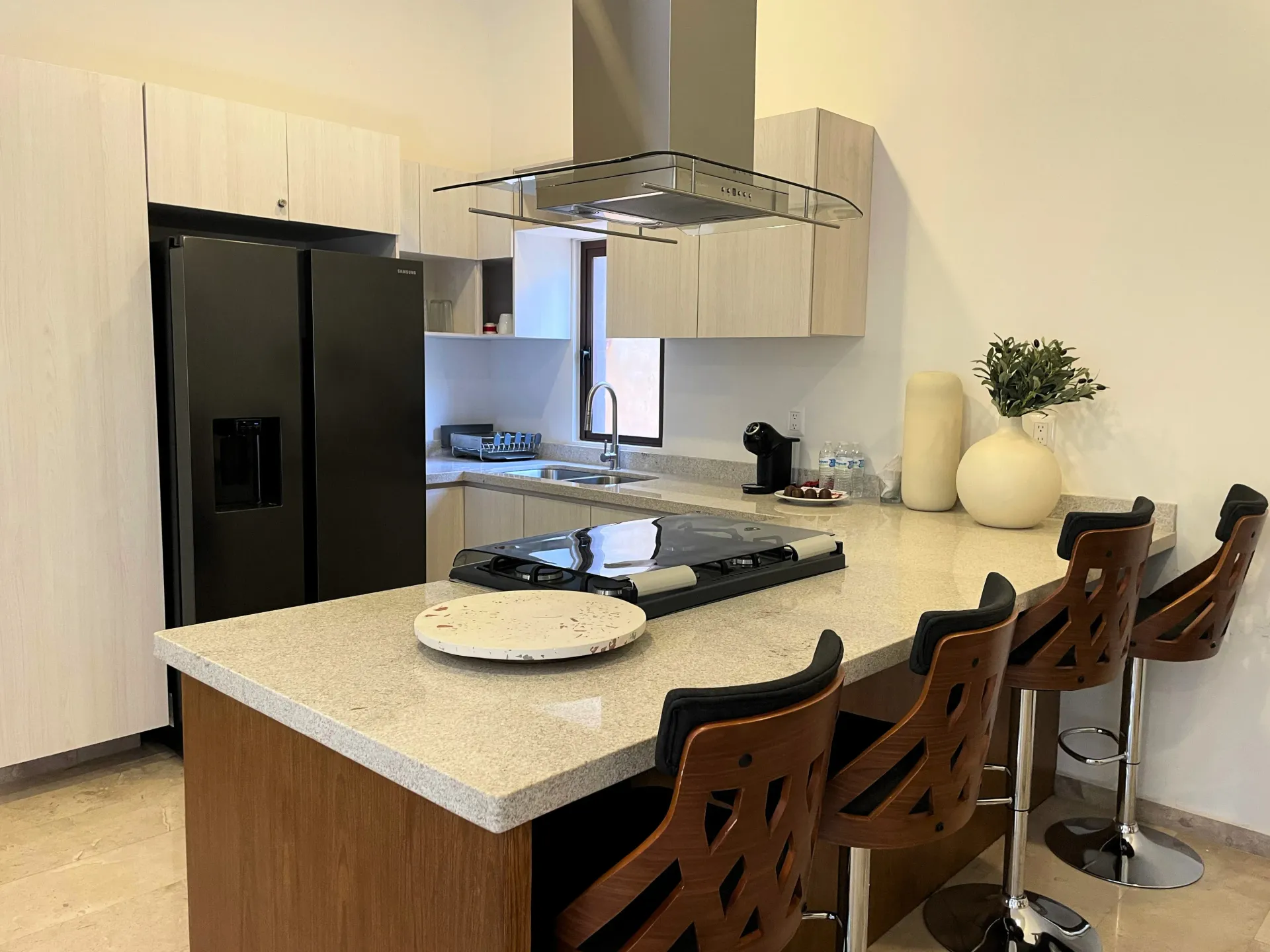 Modern kitchen with island, black refrigerator, light cabinets, and bar stools.