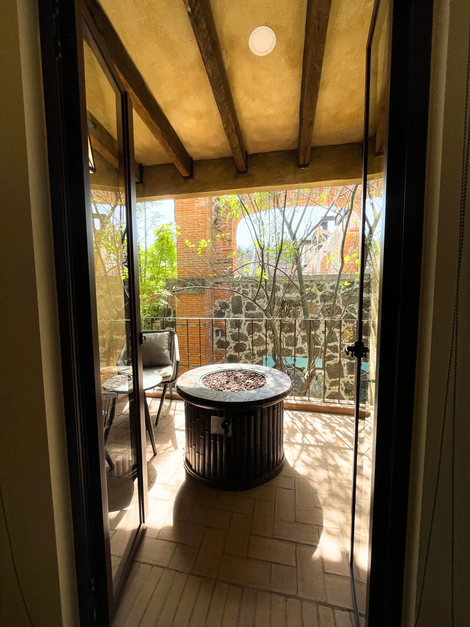 View through open doors to a balcony with a fire pit, chair, and stone wall.