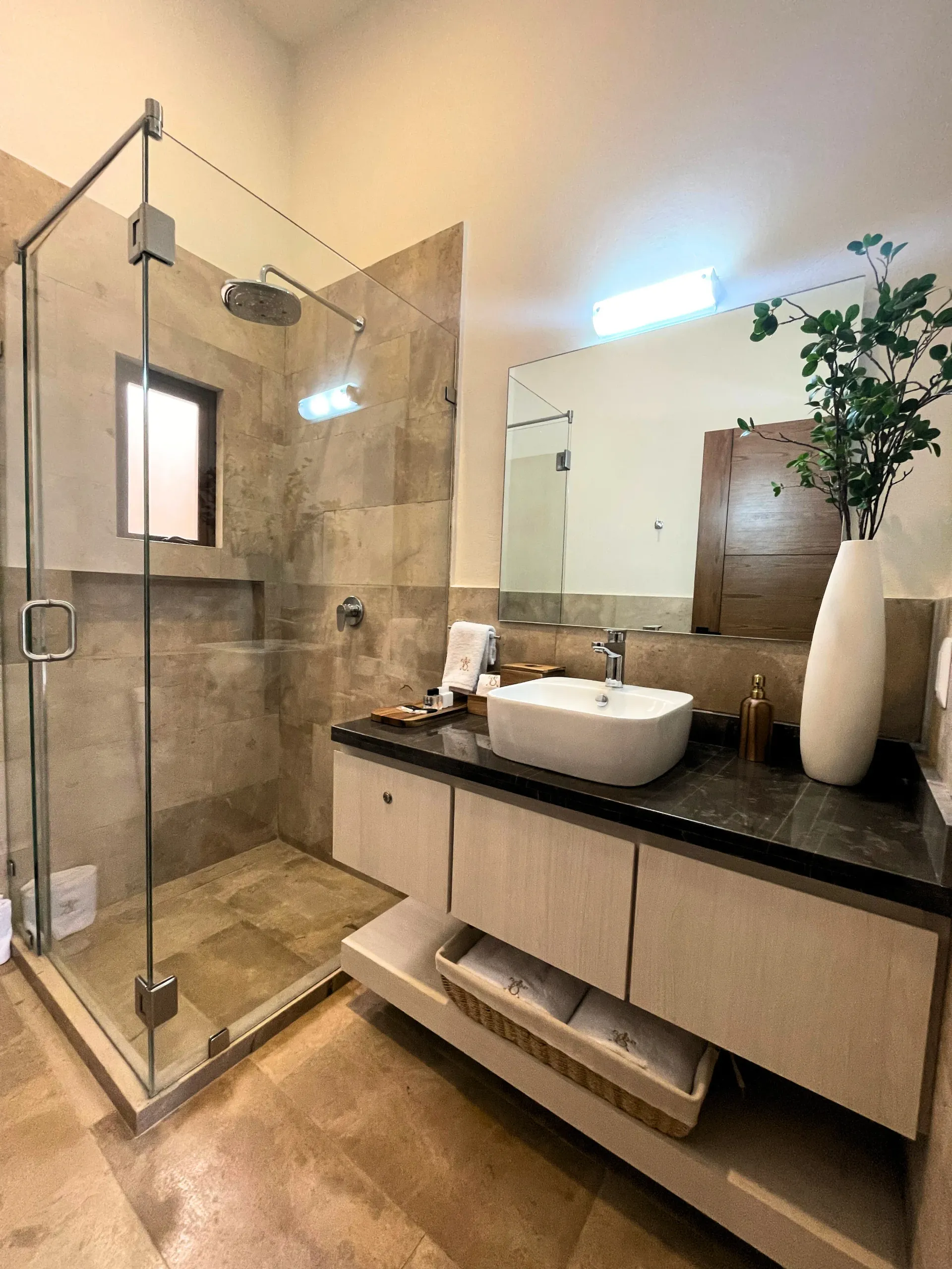 Modern bathroom with glass shower, beige tile, white sink, and wood vanity.