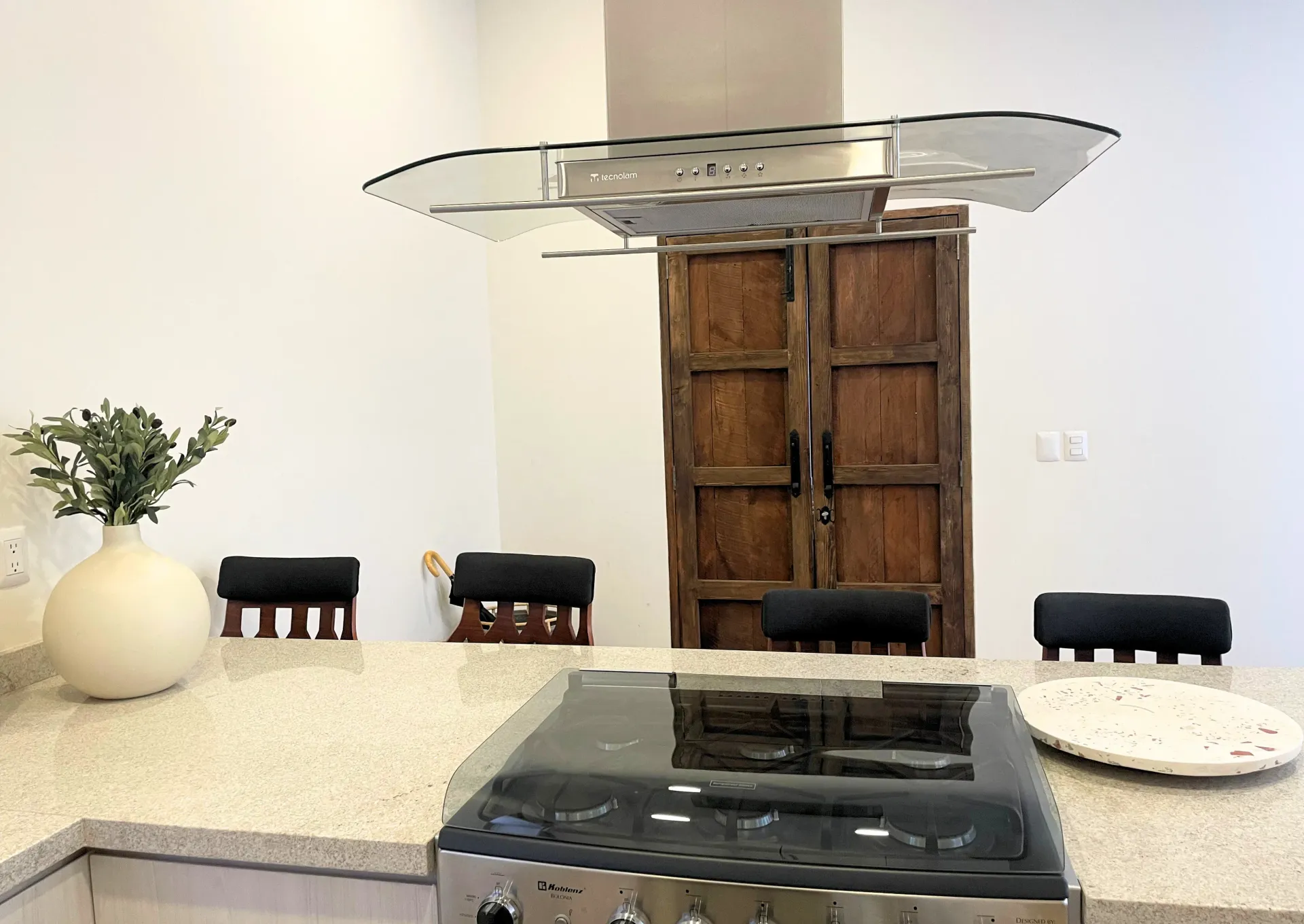 Kitchen with stove, island, chairs, vase, and a large wooden door.