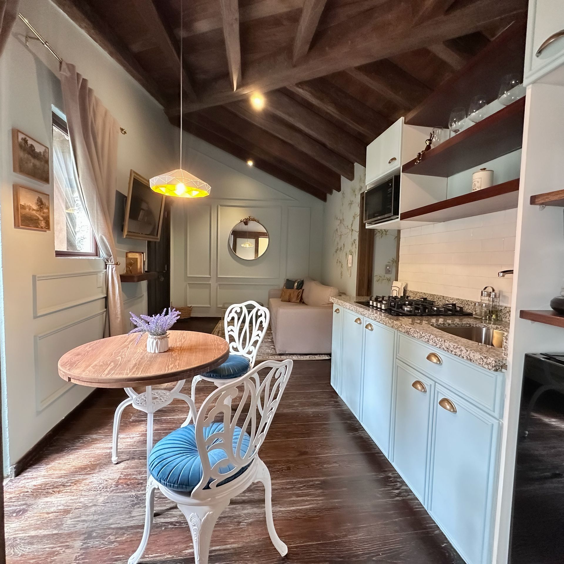 Cozy rustic kitchen with blue cabinets, round table, and hanging pendant light under wood-beamed ceiling