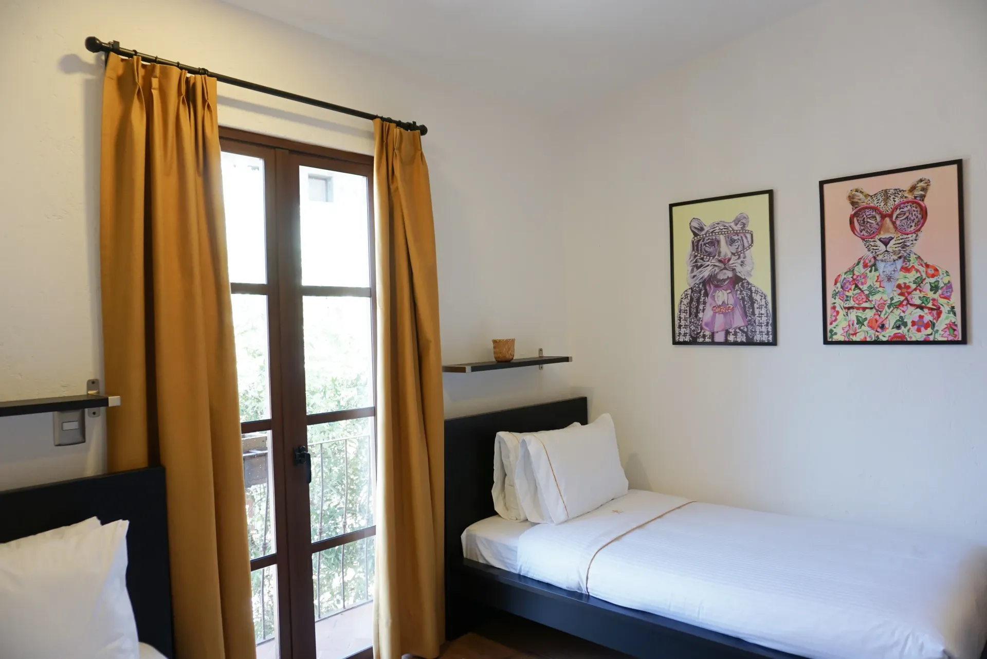 Bedroom with two twin beds, a doorway with yellow curtains, and two framed art pieces on the wall.