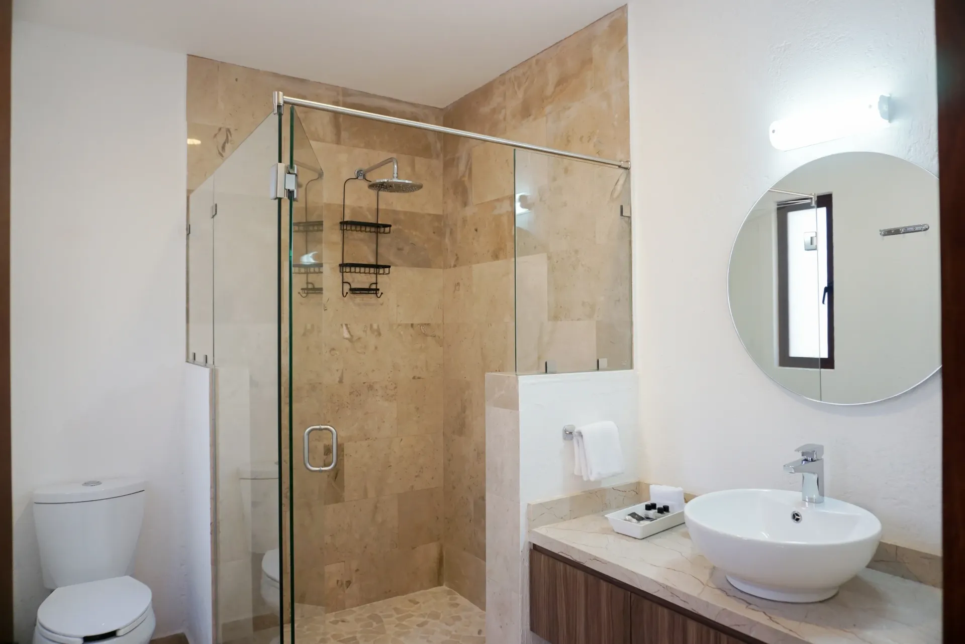 Bathroom with a glass shower, toilet, vanity with a round mirror.