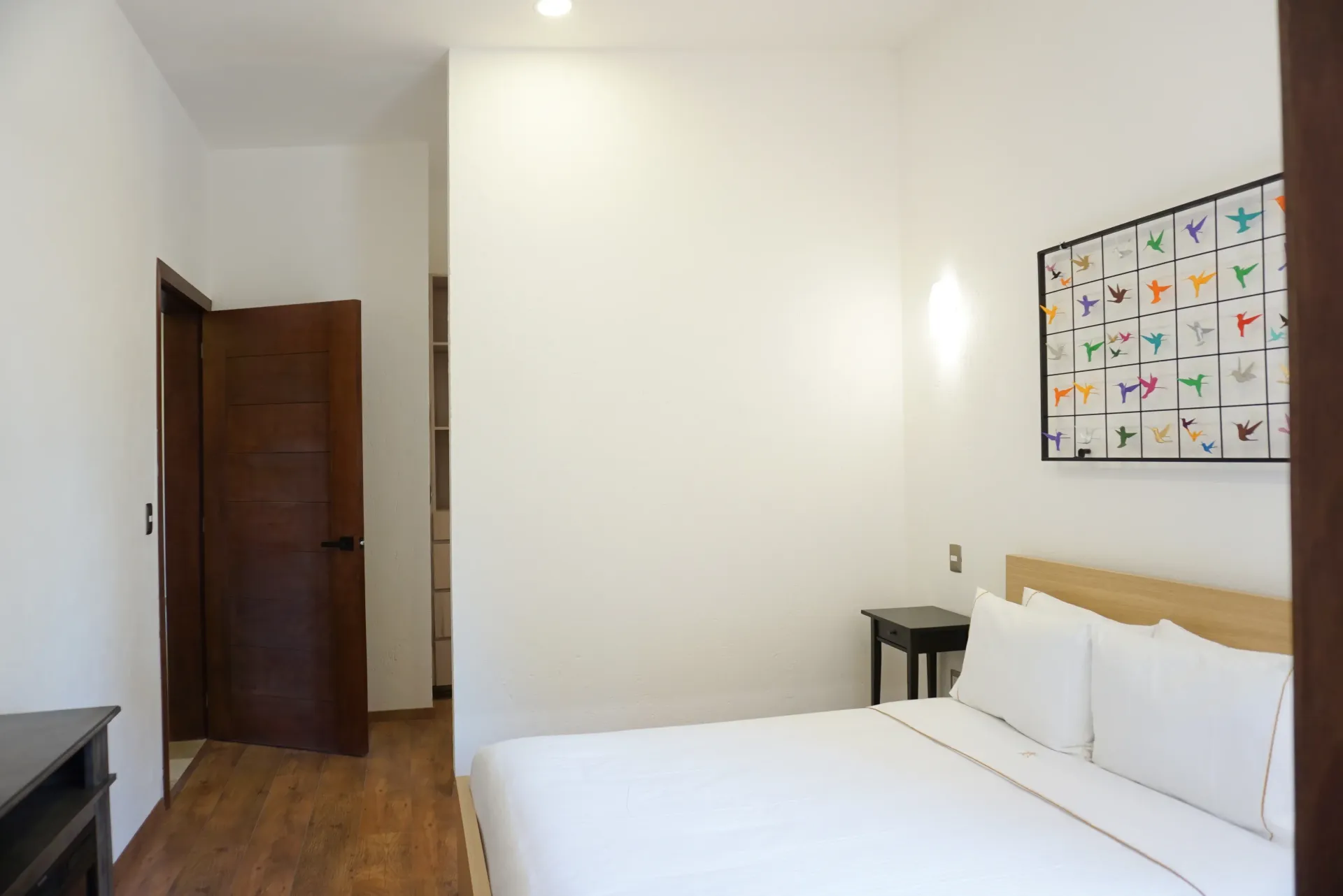 Bedroom with white walls, bed, wooden door, and abstract art.