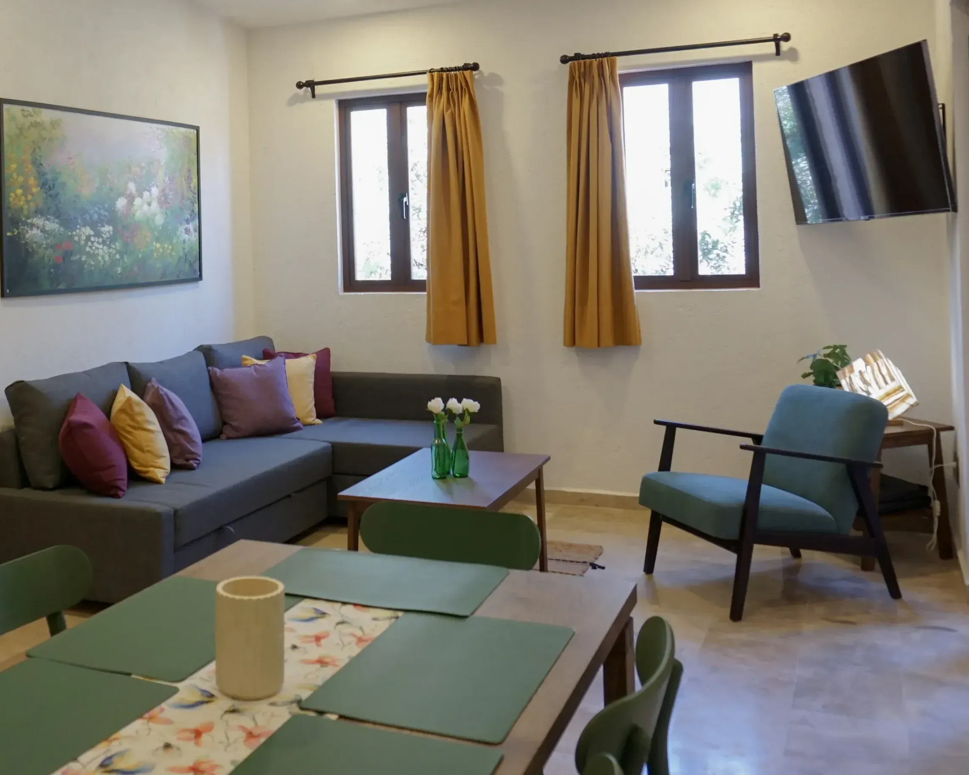 Sala de estar con un sofá seccional gris, una silla verde azulado y una mesa de comedor.