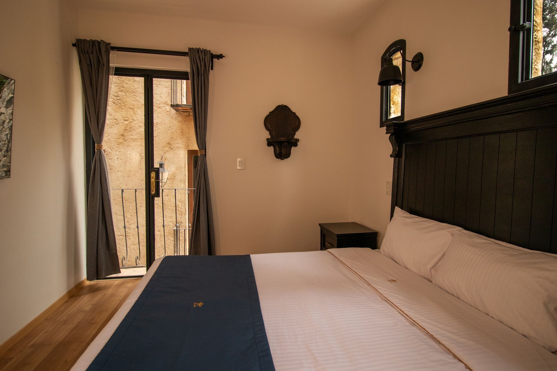 Bedroom with a large bed, blue runner, dark curtains, and a doorway to a balcony.