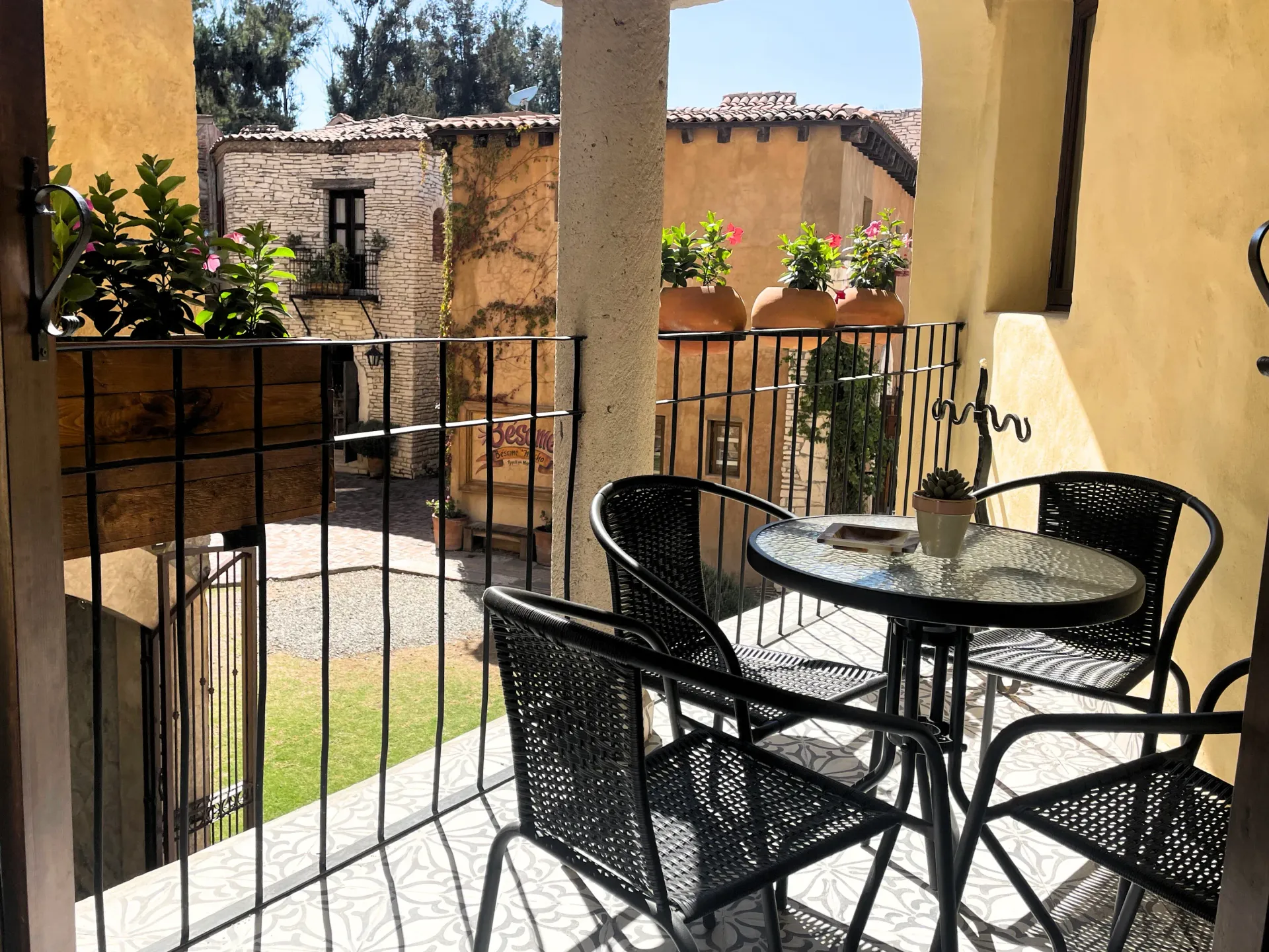 Balcony with table and chairs, overlooking a courtyard with stone buildings and potted plants.