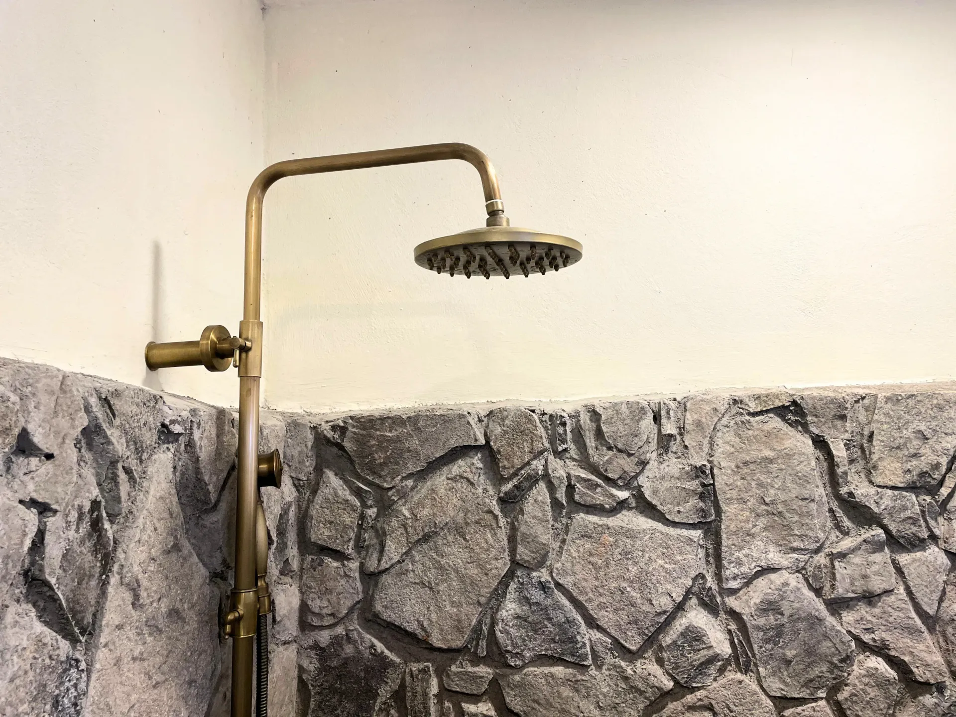 Shower with brass fixtures set against a stone wall.