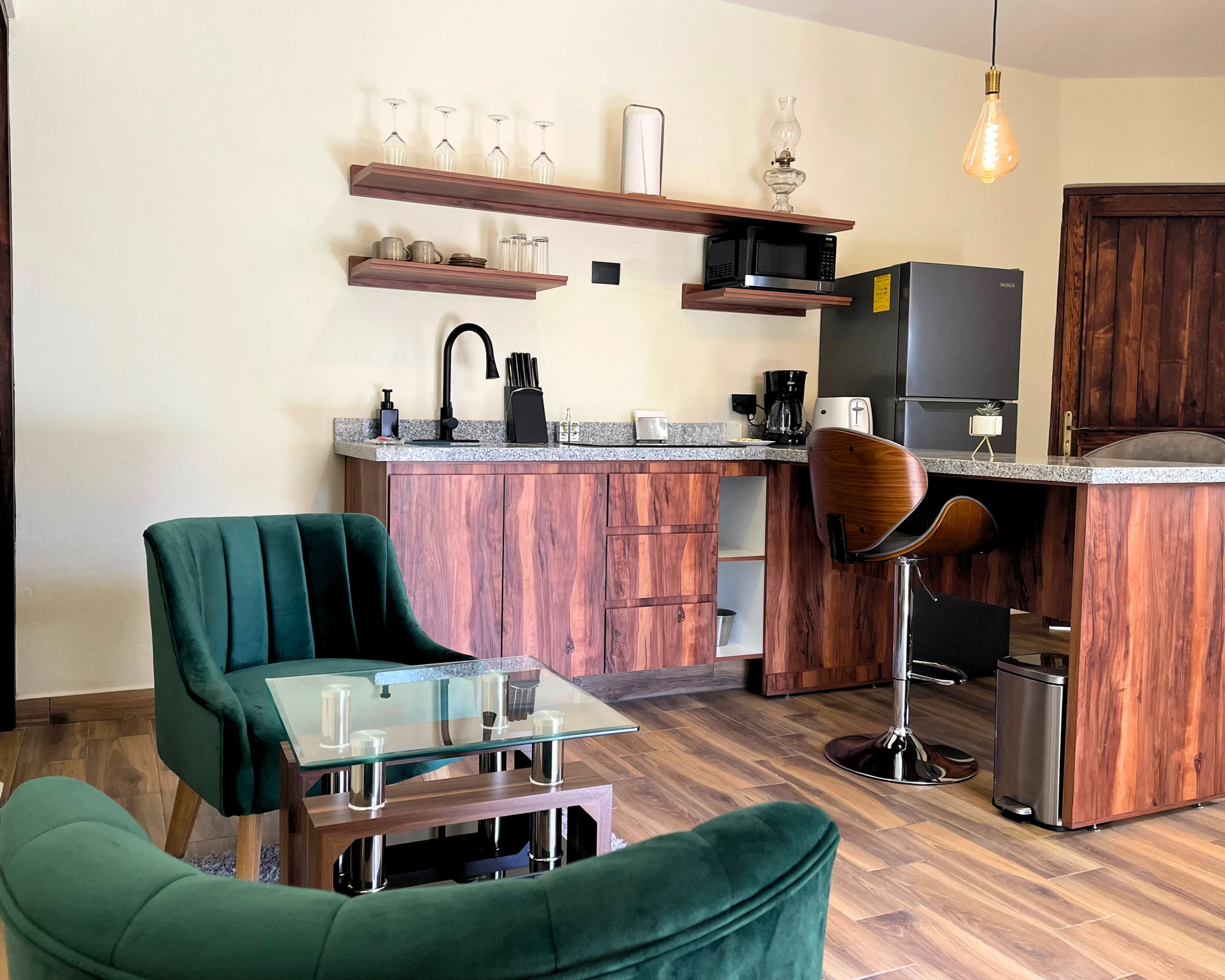 Una cocina moderna con gabinetes de madera, encimeras de granito y una silla de terciopelo verde.
