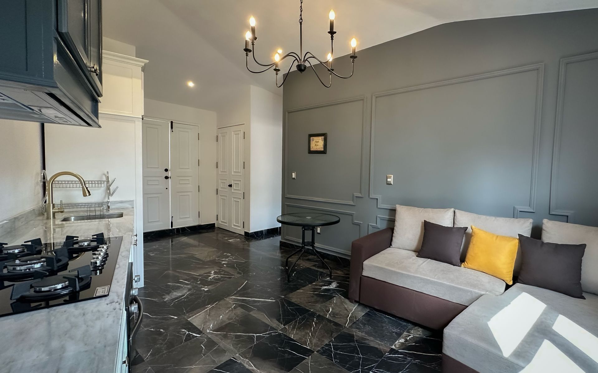 Modern gray living room with dark marble floor, gray sofa, chandelier, and open kitchen area