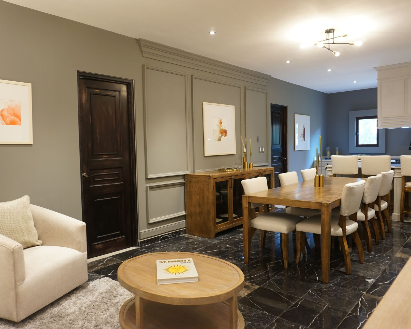 Una moderna sala de estar y comedor con una mesa y sillas de madera, un sofá beige y pisos oscuros.