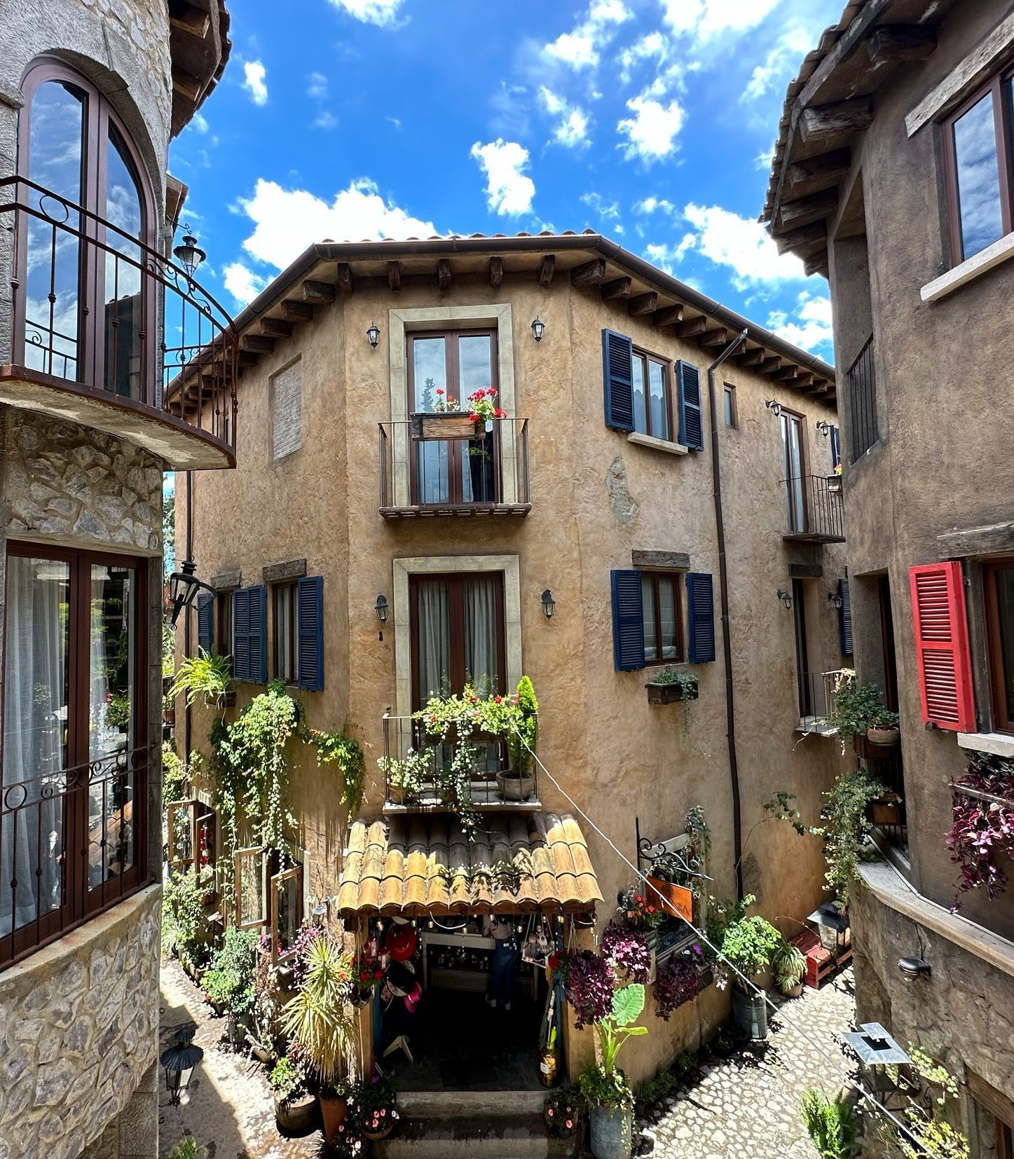 European-style buildings with stucco walls and arched windows, adorned with plants, under a blue sky with clouds.