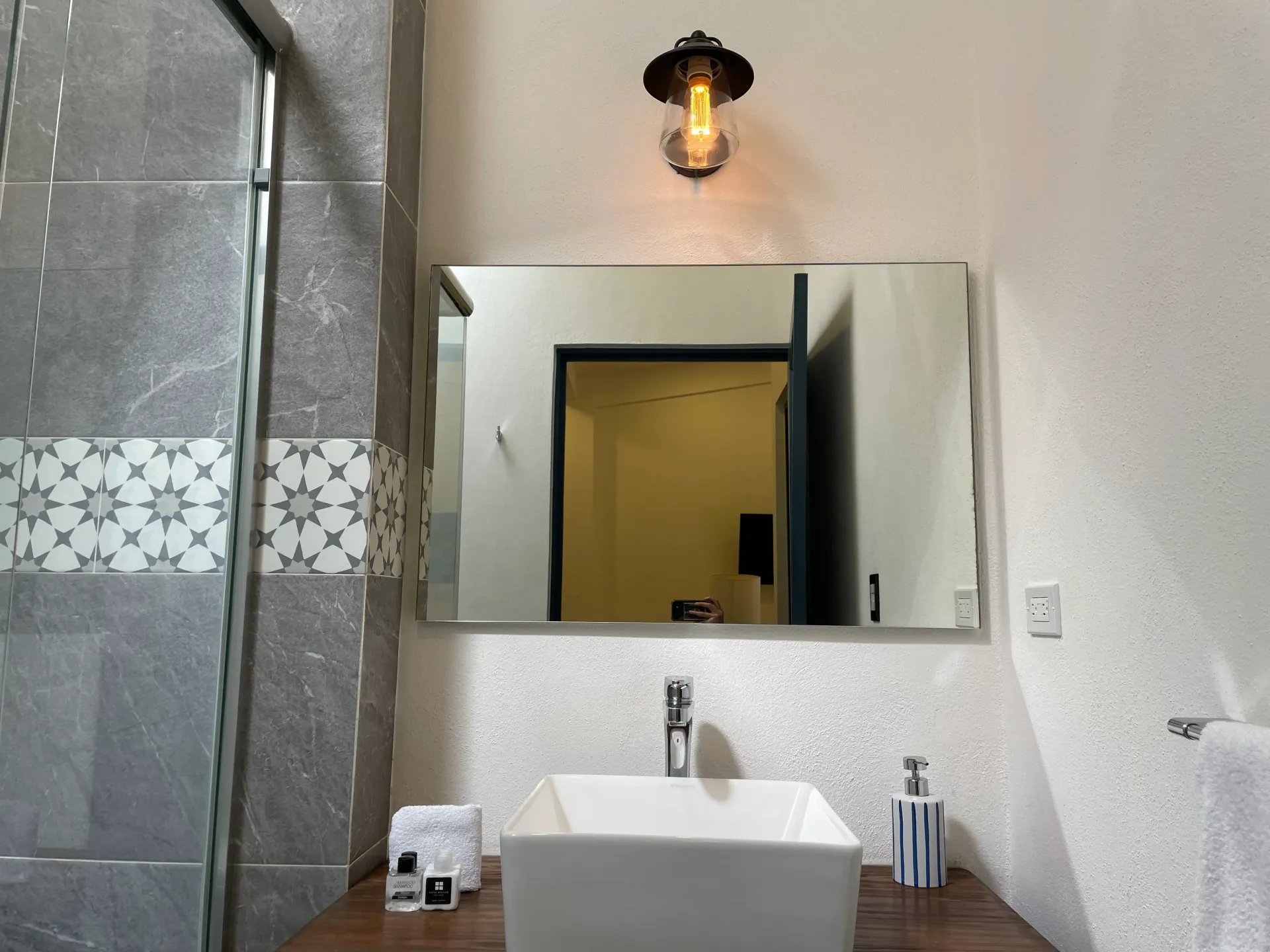 Bathroom with square sink, mirror, light fixture, shower, and decorative tile.
