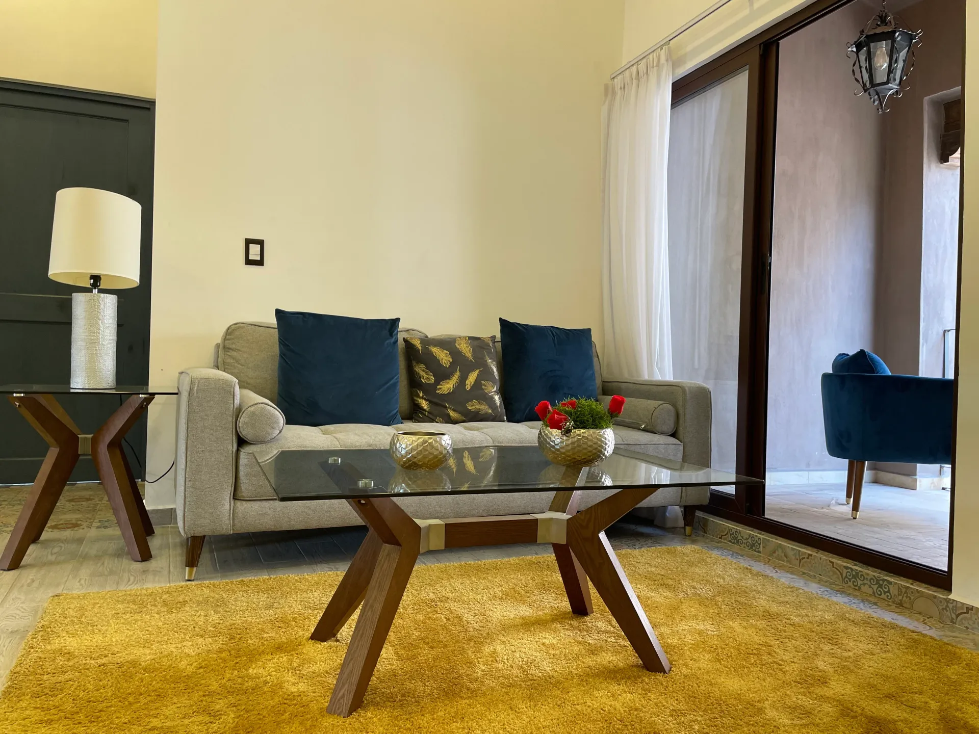 Living room with gray couch, glass coffee table, yellow rug, and balcony access.